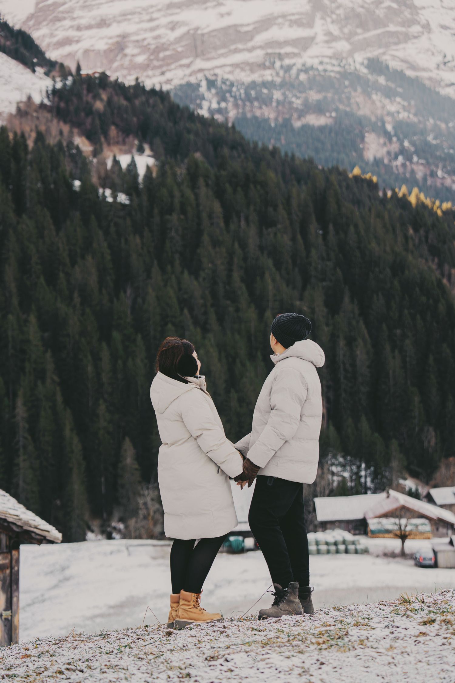 Couple holding hands gazing at snow-covered mountain forest landscape in winter Alps.