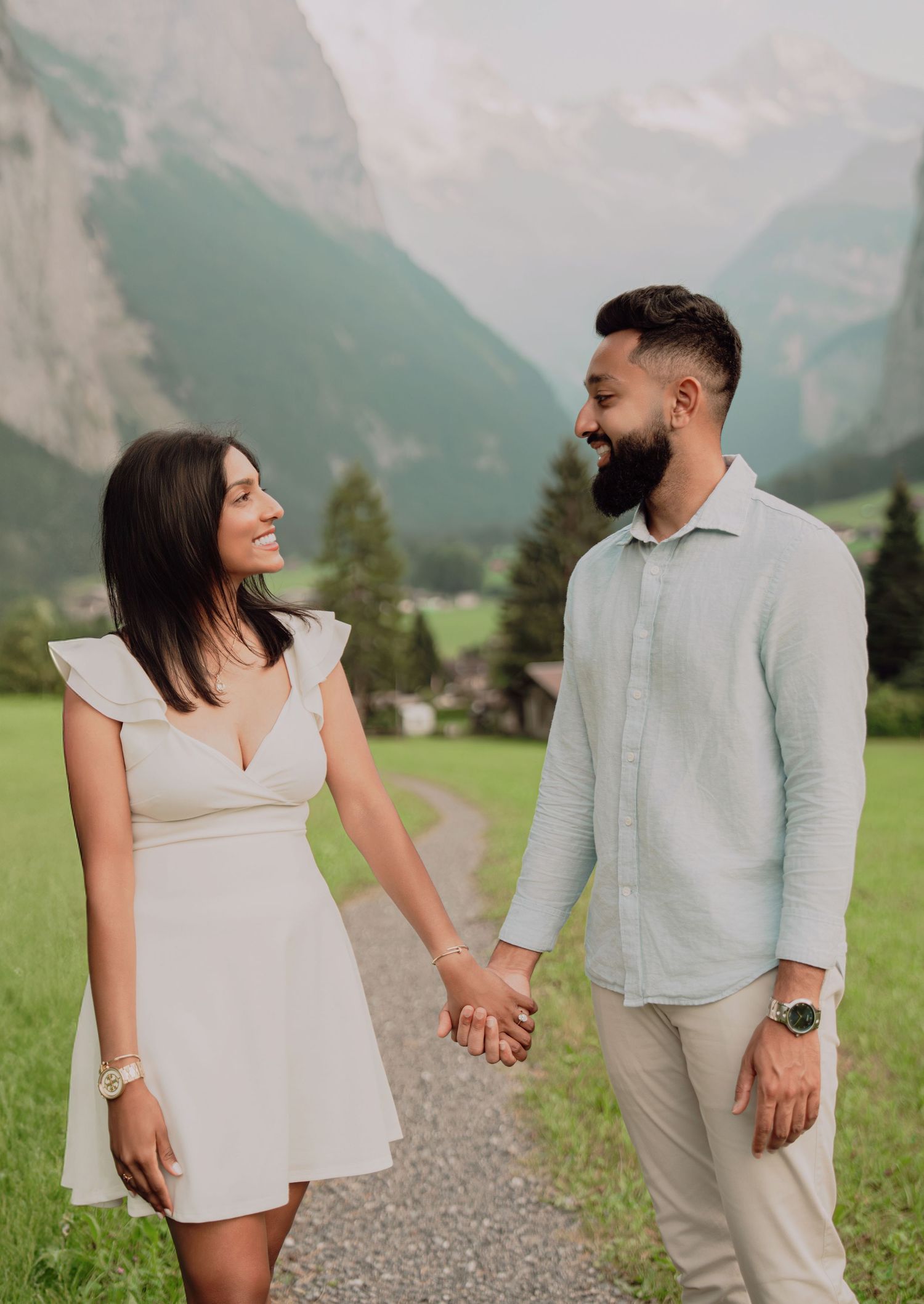Joyful couple holding hands and smiling at each other on a scenic Alpine path in Switzerland.