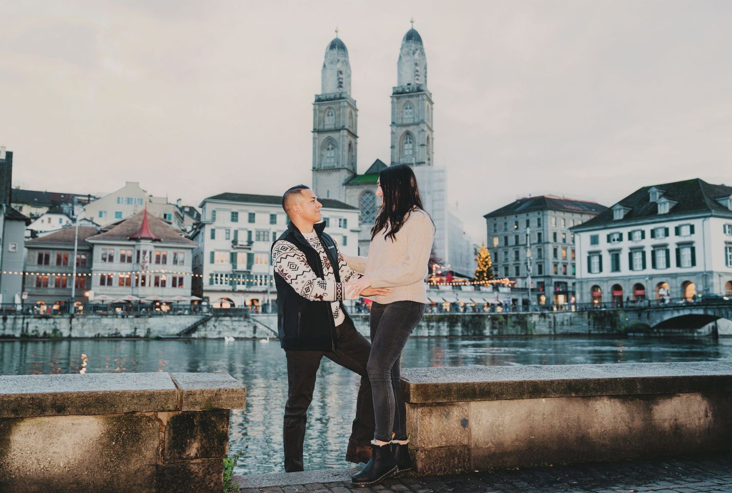 Romantic couple facing each other by the Limmat River with Grossmünster twin towers in Zurich.
