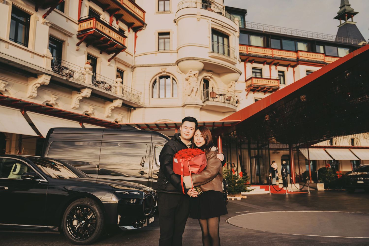 Couple embracing in front of luxury European hotel with black car nearby.