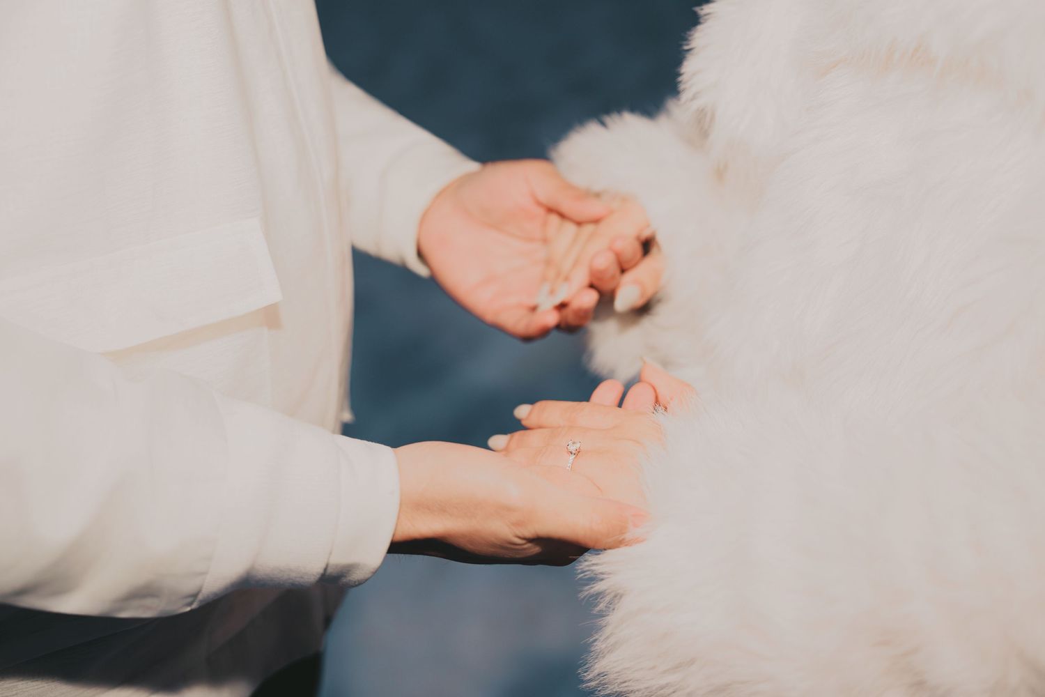 Close-up of couple exchanging rings with white fur coat detail visible during winter engagement ceremony.