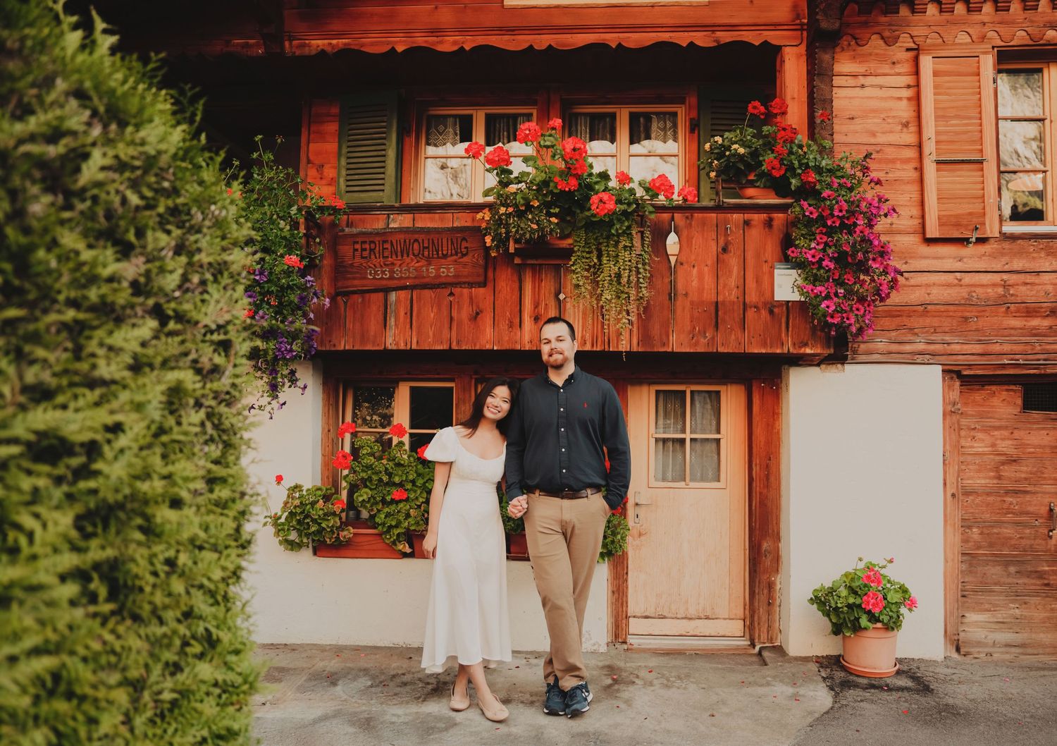 Couple smiling together outside a traditional Swiss wooden chalet adorned with colorful flowers.