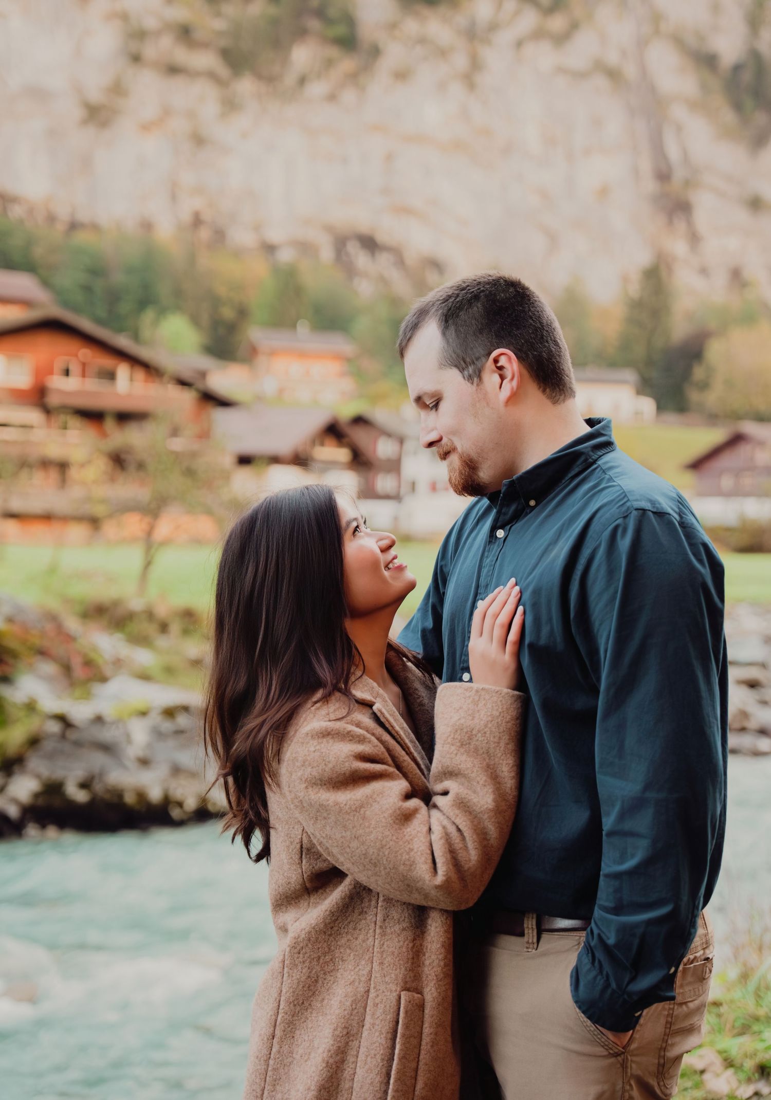 Couple sharing a romantic moment by a glacial river with Swiss mountain village backdrop.