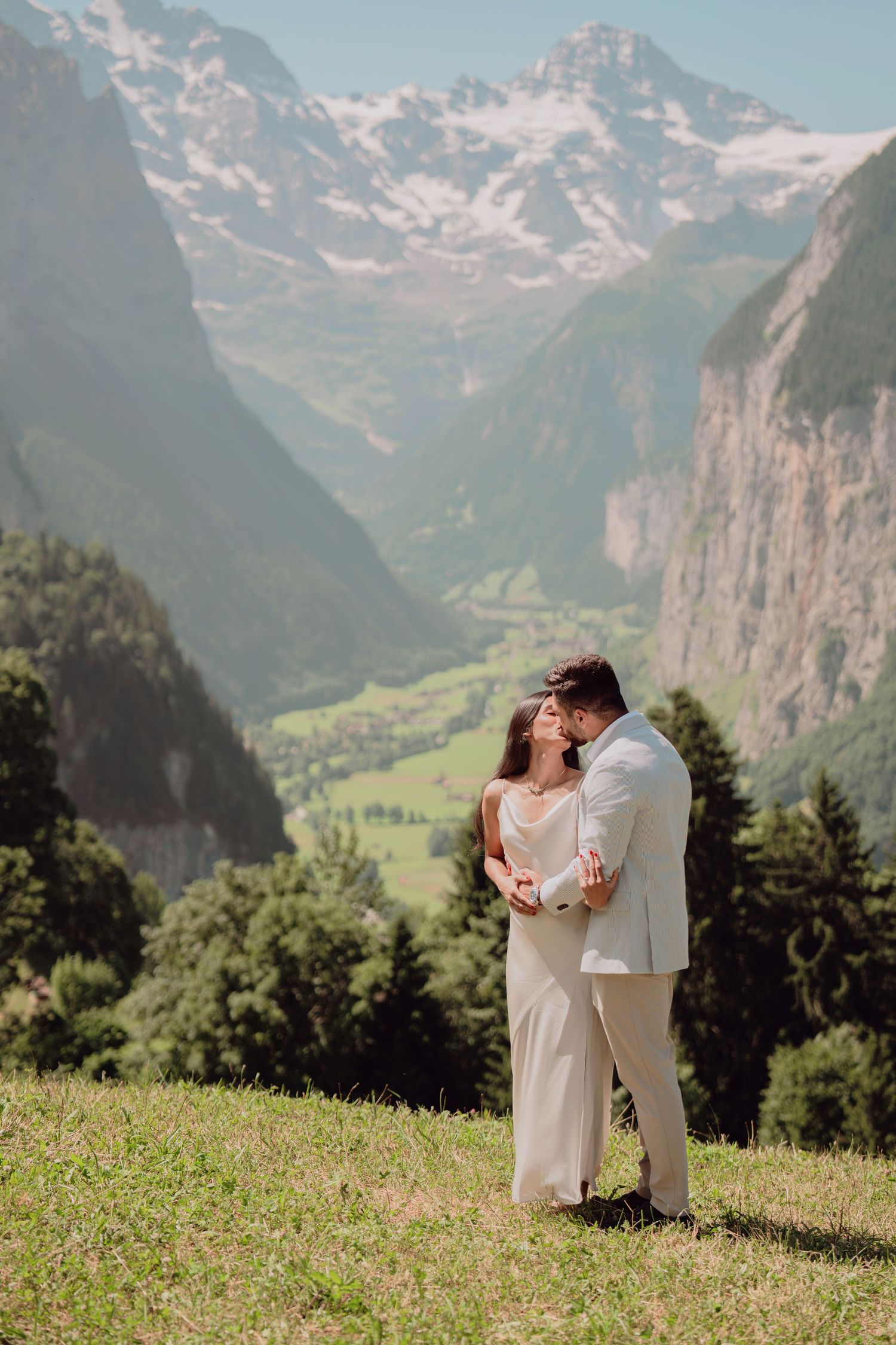 Elegant couple embracing on a mountain meadow with breathtaking Lauterbrunnen valley and snow-capped peaks behind them.