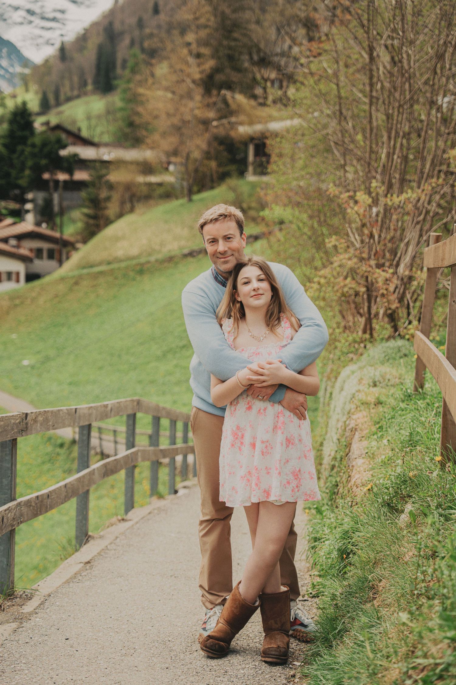 A couple embraces on a scenic alpine path surrounded by green meadows and traditional Swiss chalets.