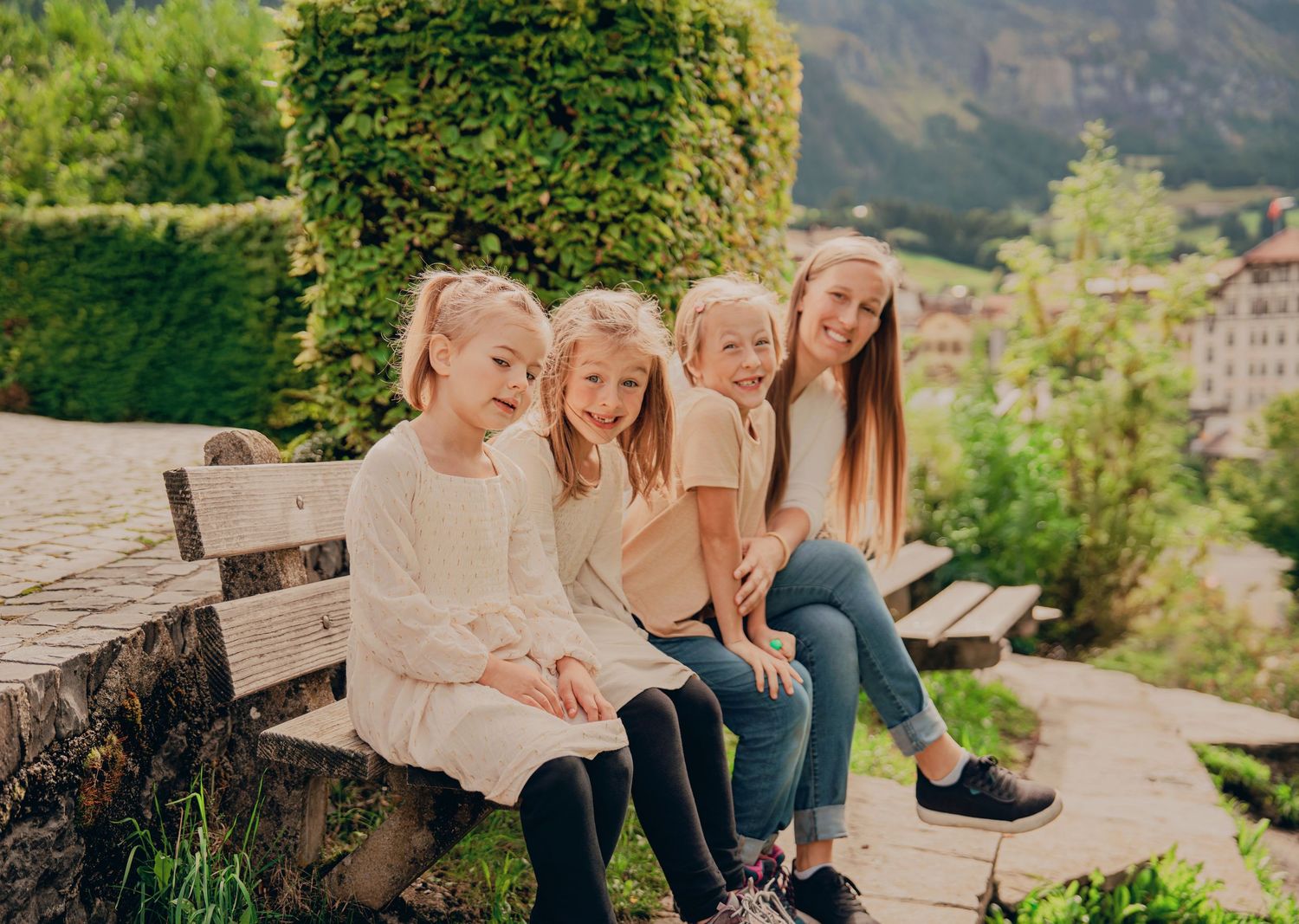 Four girls sitting together on a bench smiling in a charming Swiss town garden.
