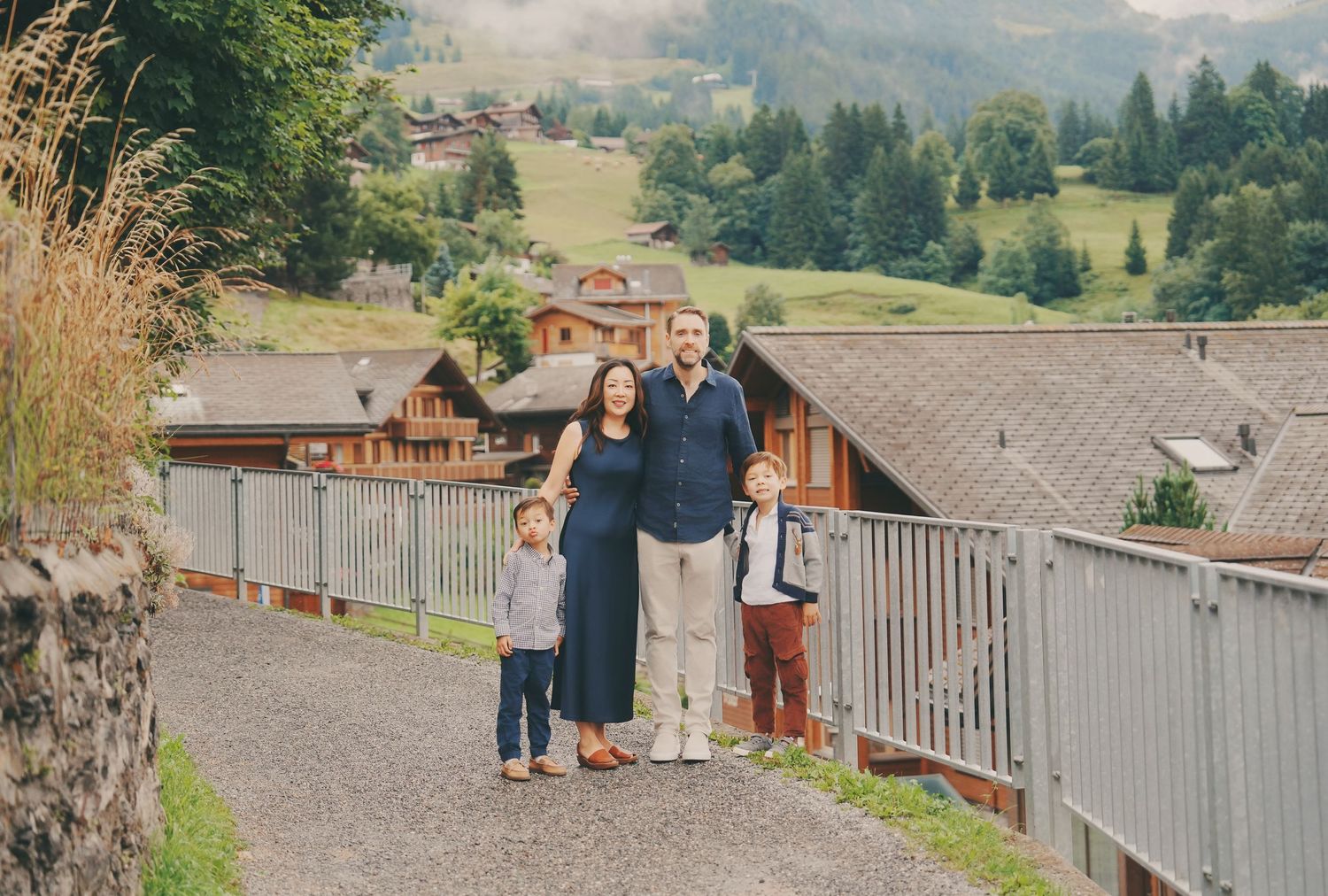 Family of four standing close together on a gravel path with Swiss chalet village in background.