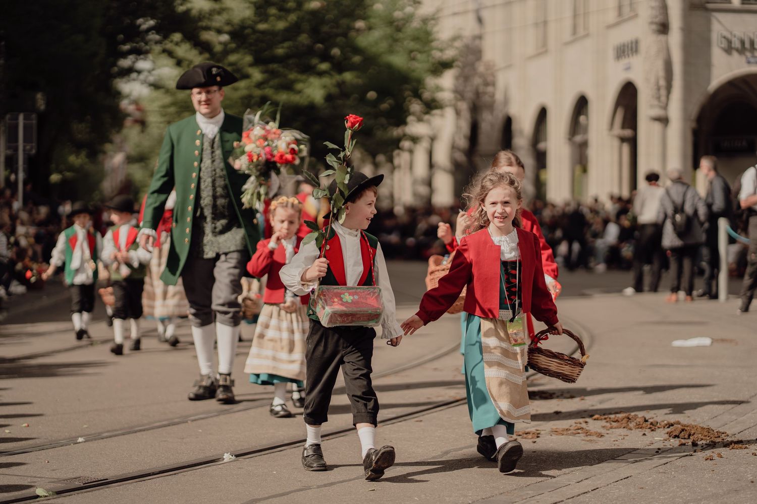 Children in traditional folk costumes walk hand-in-hand during a colorful festival parade.