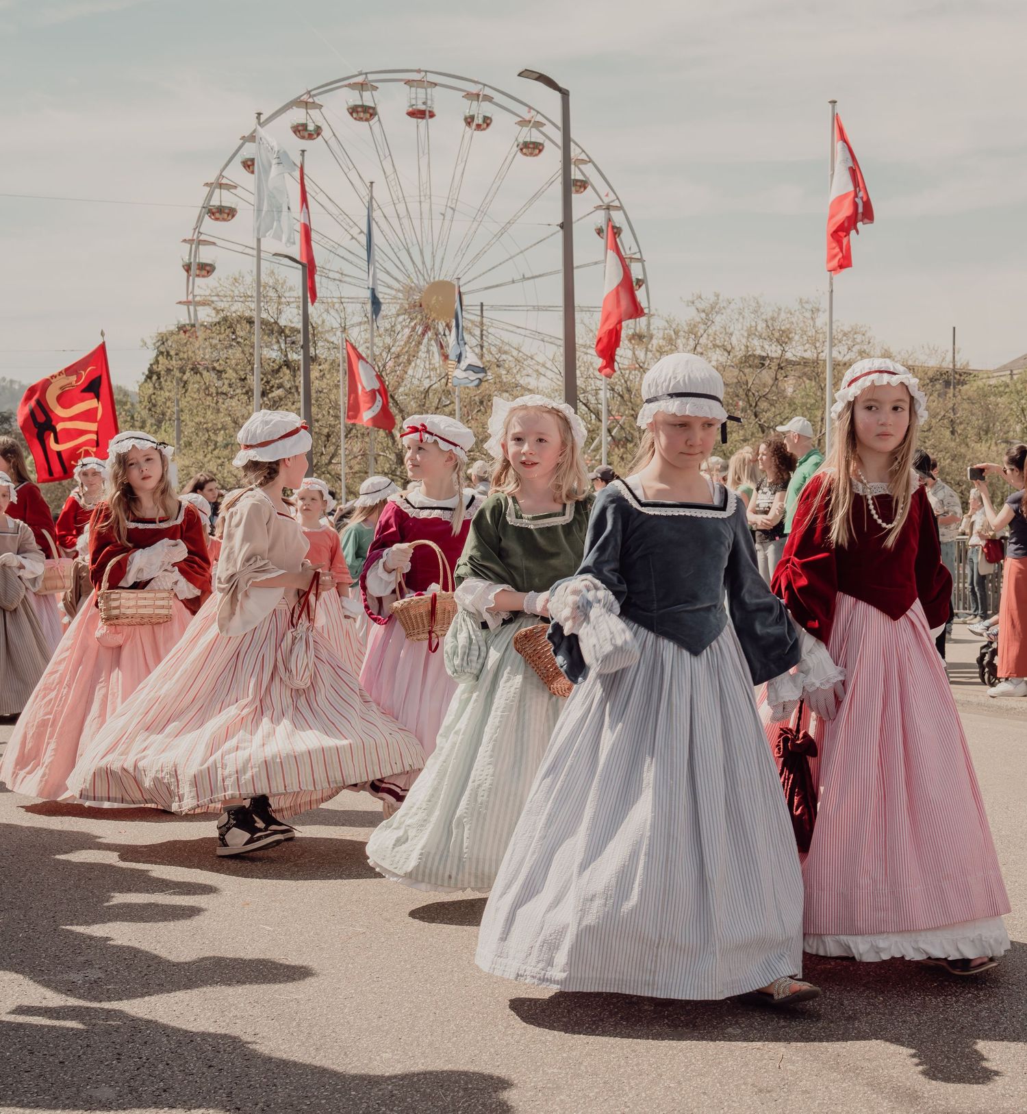 Girls in colorful historical period costumes marching in parade near ferris wheel.
