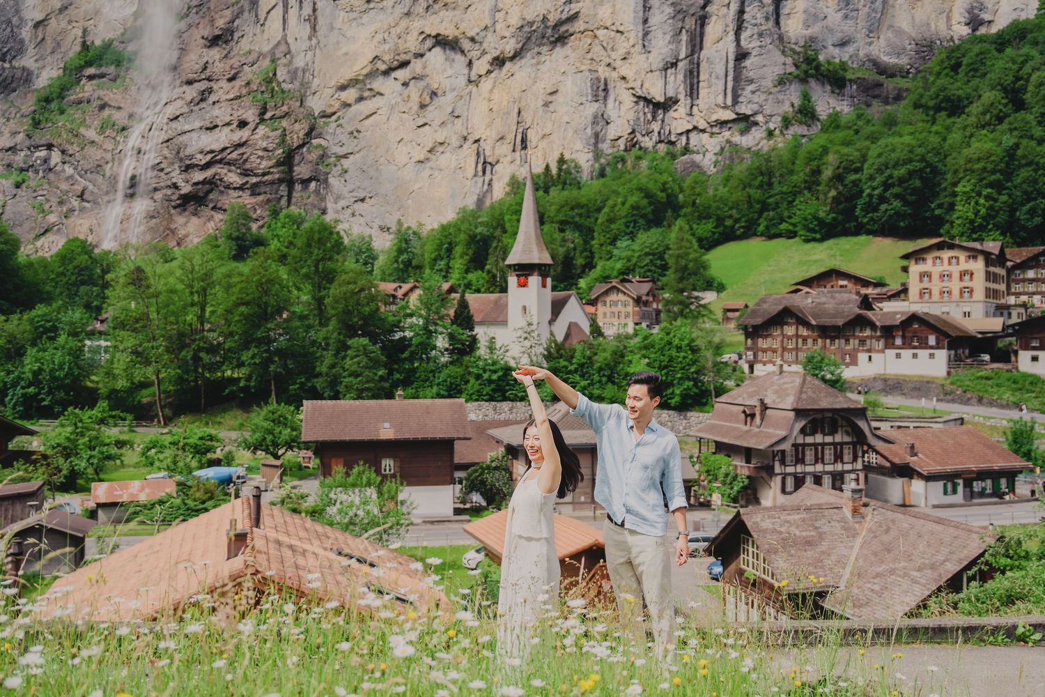 Joyful couple celebrating with raised arms in a flower field with Lauterbrunnen Swiss village backdrop.