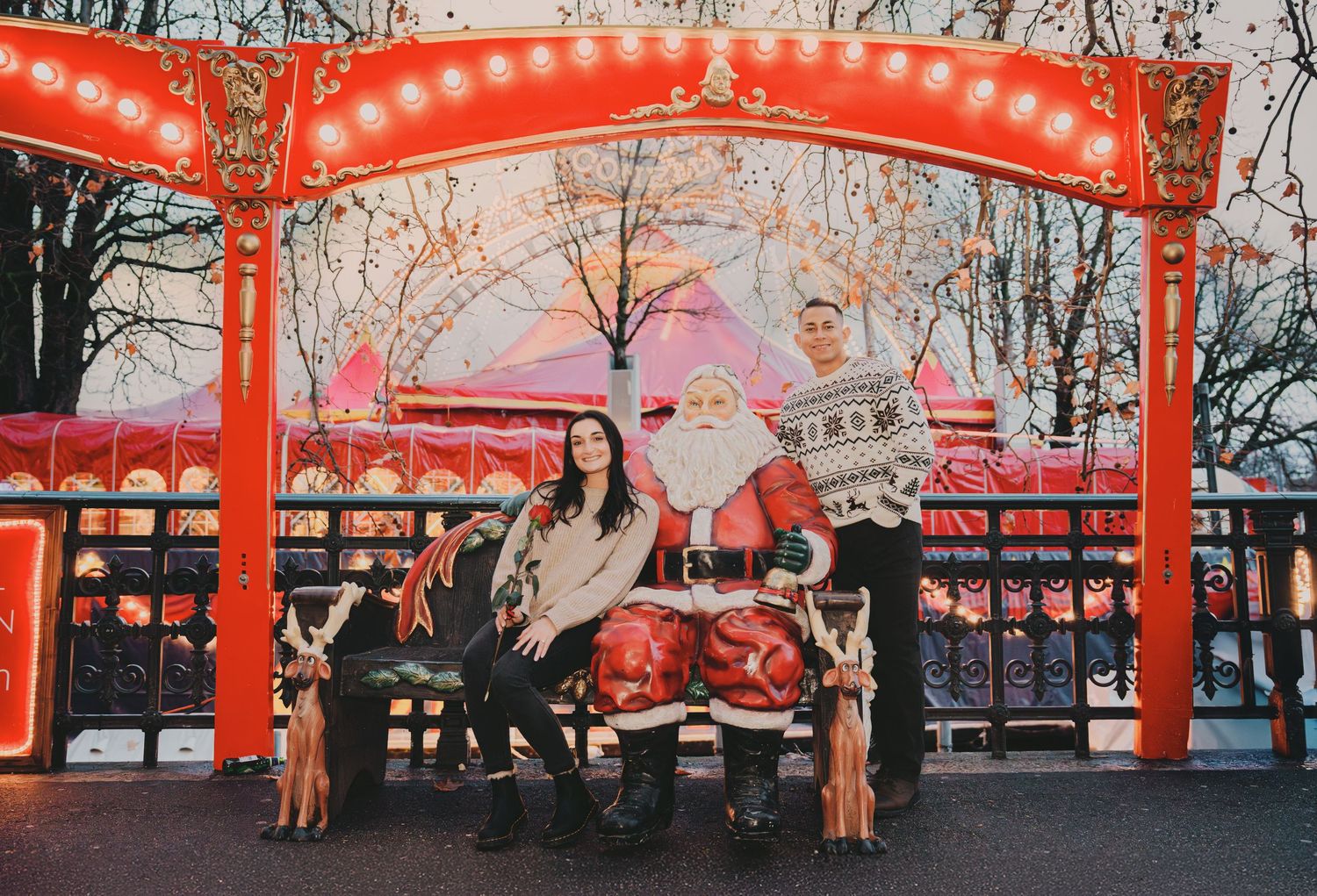 Couple sitting with Santa Claus under a red ornate arch at a Christmas fair.