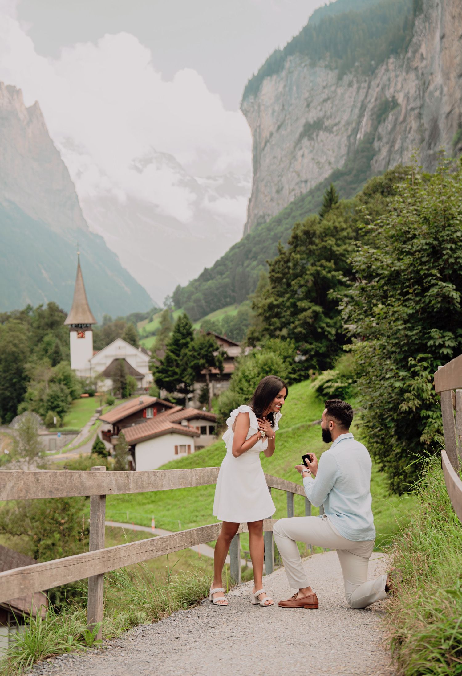 Man proposes to woman on one knee on a scenic mountain path in Lauterbrunnen, Switzerland.