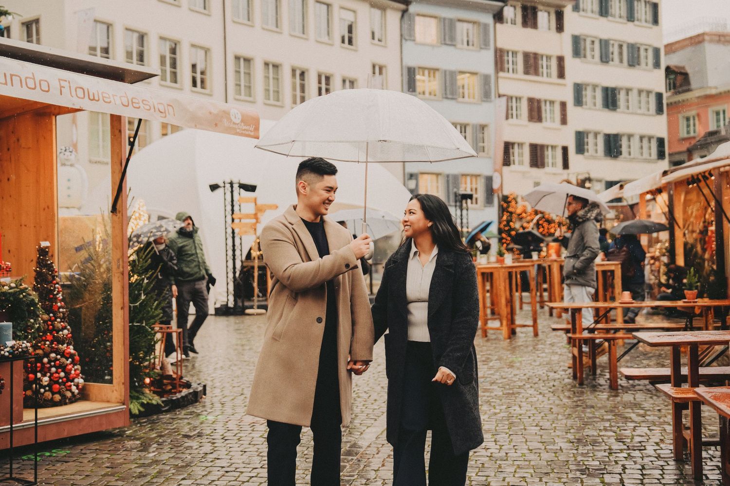 Couple sharing umbrella chatting at rainy outdoor Christmas market.