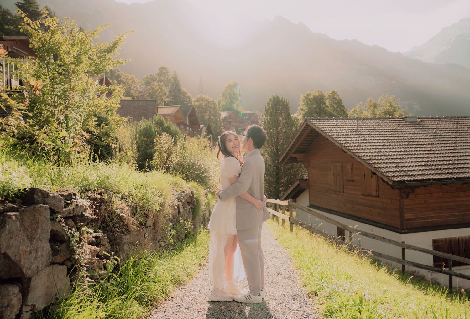 Couple sharing a tender embrace on a hillside path in a misty Swiss alpine village at sunrise.