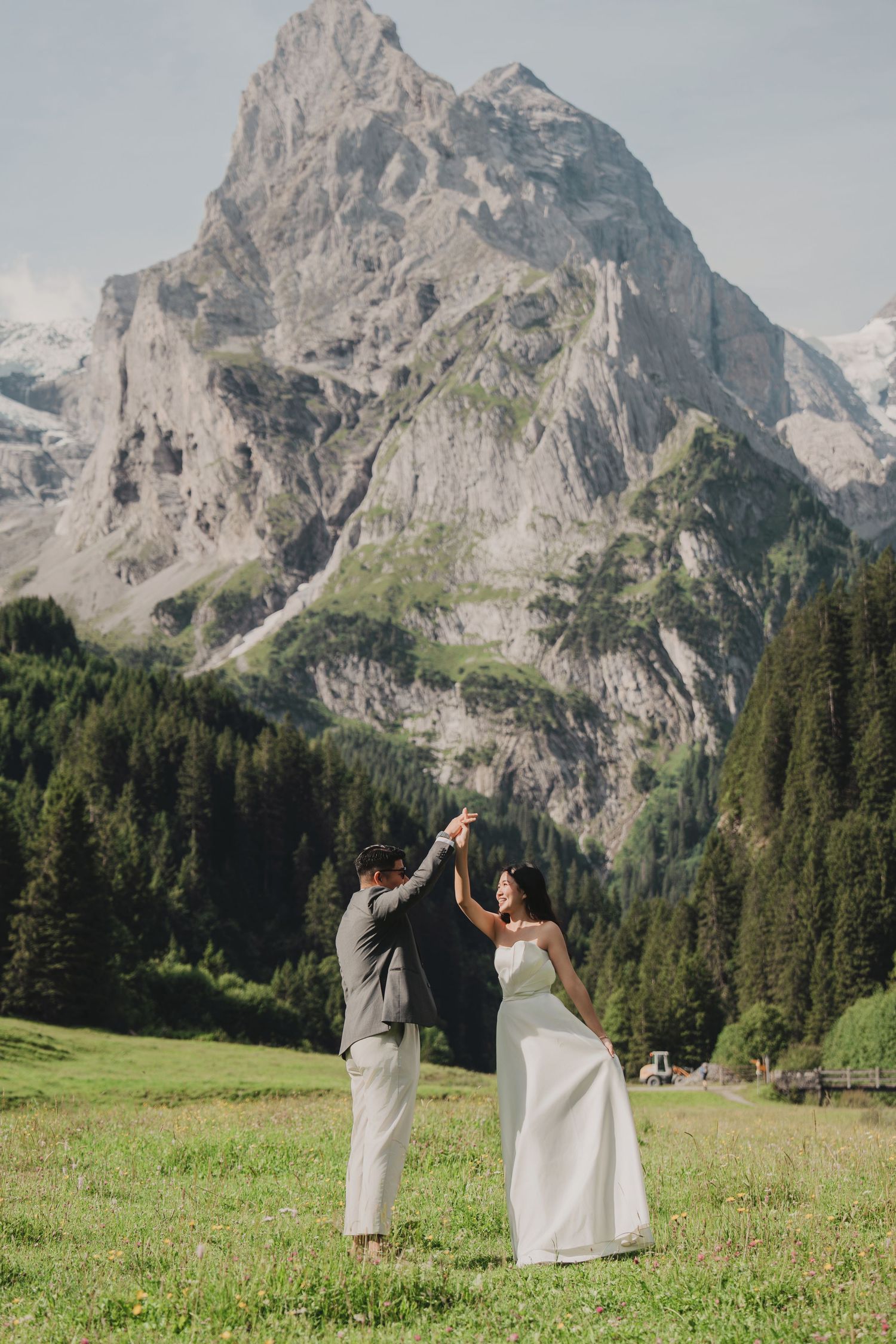 Bride and groom dancing in alpine meadow with dramatic mountain peak backdrop during outdoor wedding.