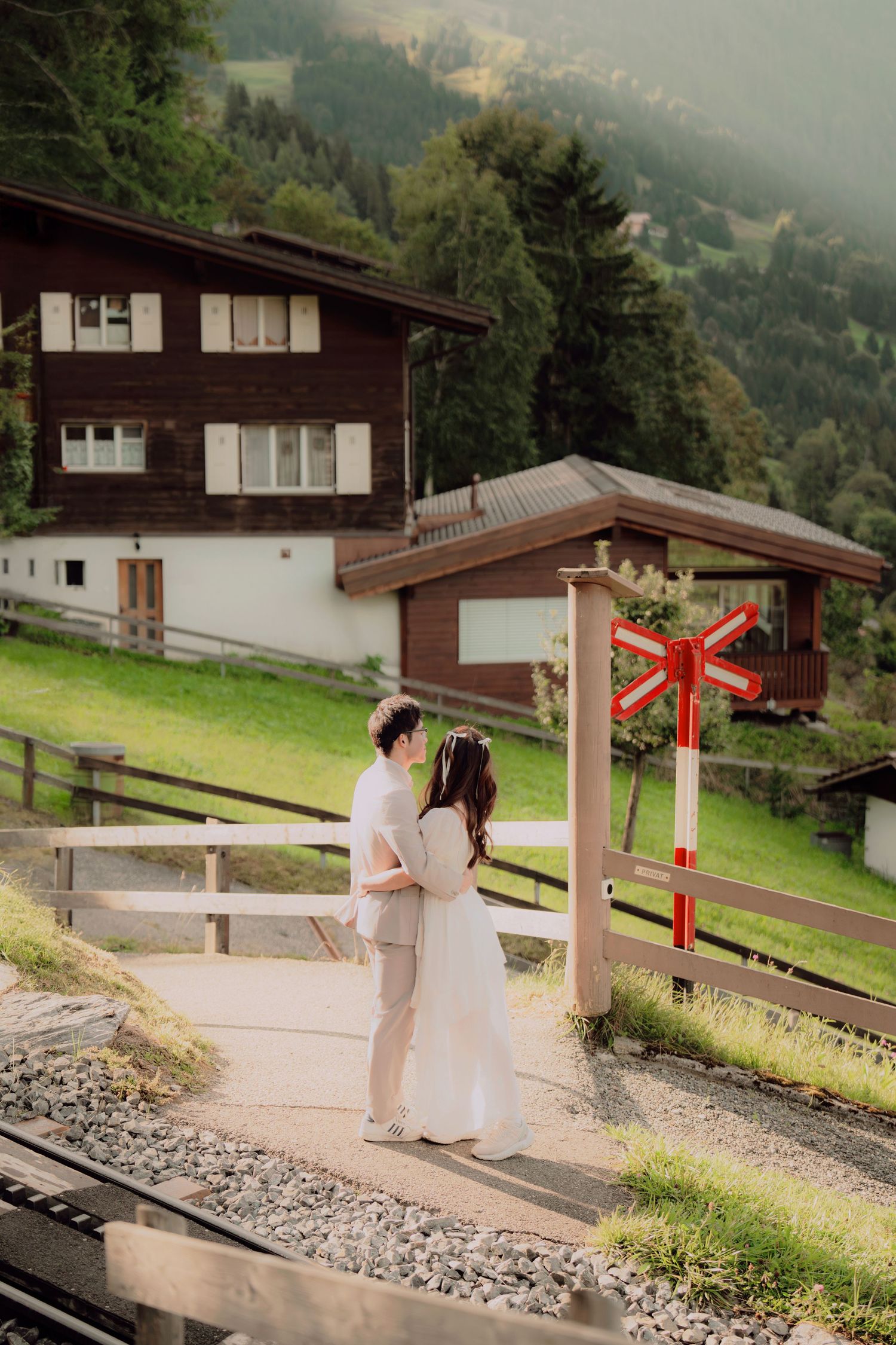 Couple in wedding attire sharing a romantic moment by a railway crossing in a scenic Swiss Alpine village.