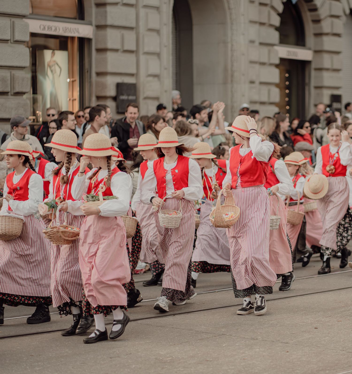 Group of women in red and pink Swiss folk costumes carrying baskets in a festive parade.