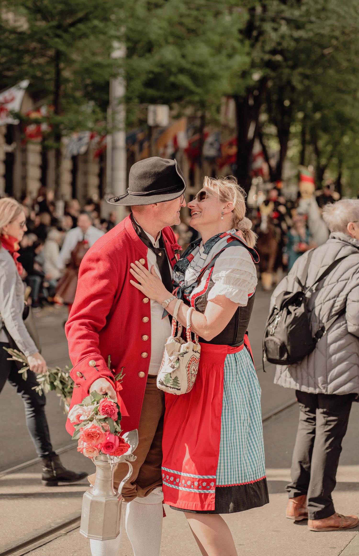 Couple in traditional Bavarian costumes share a romantic moment during a festive street parade.