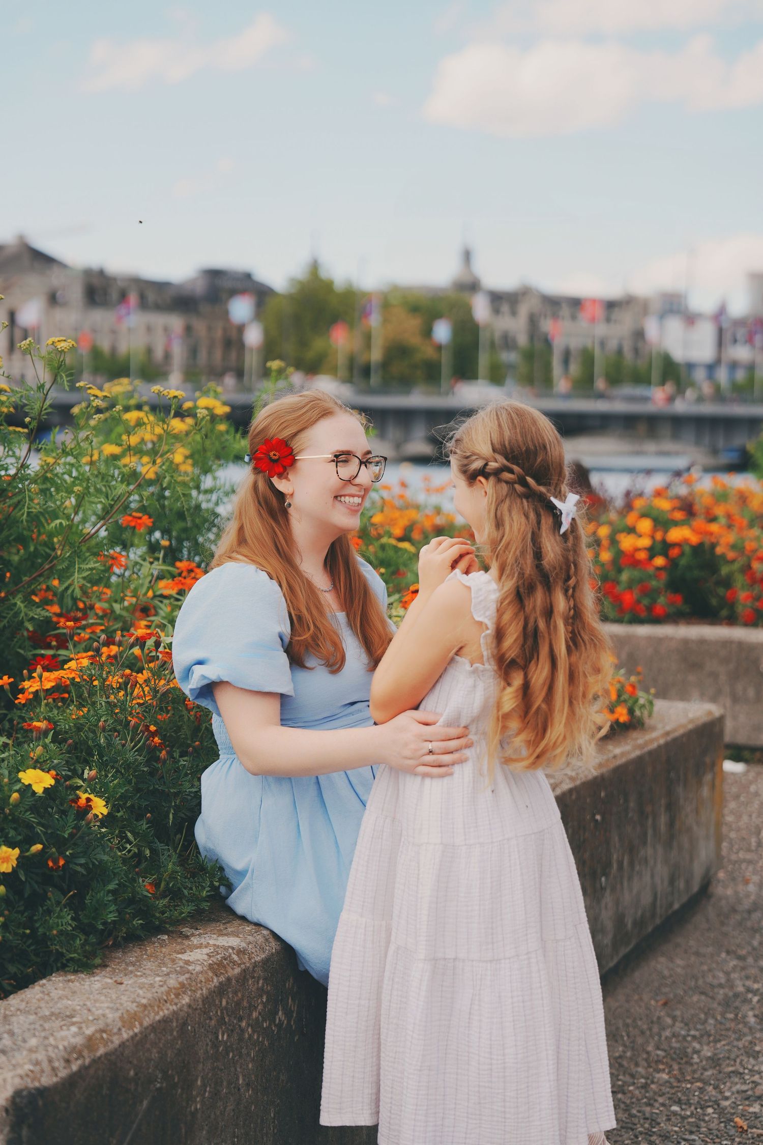 Two girls laughing together among bright orange flowers by the Zurich waterfront on a sunny day.