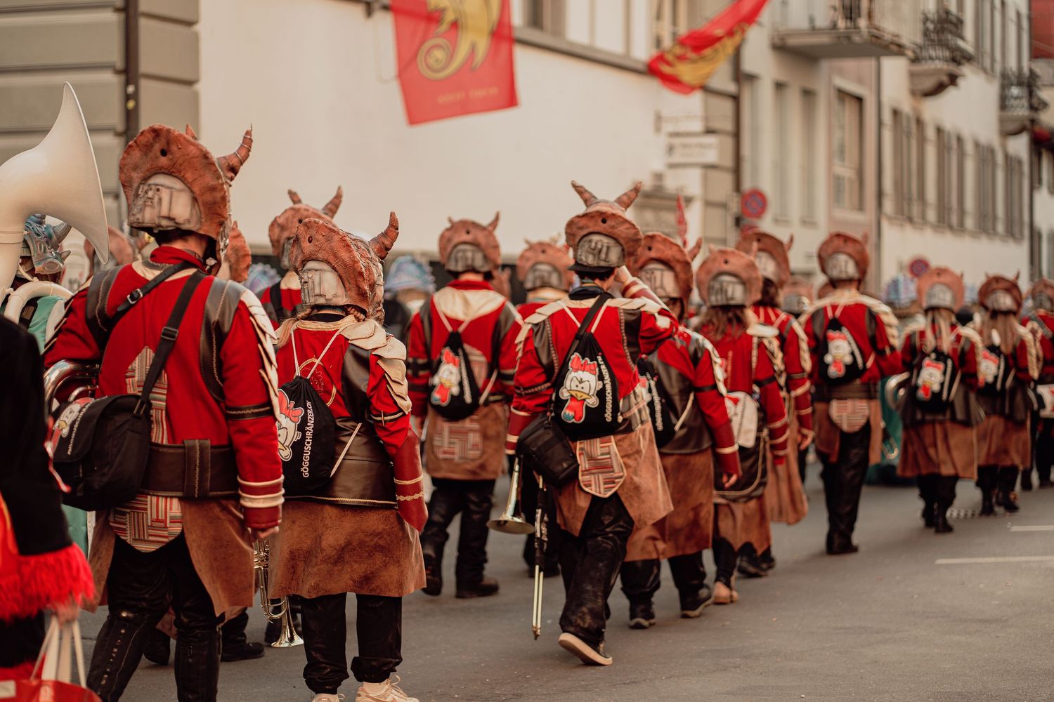 Group of performers in red medieval costumes with animal masks march in a street parade.