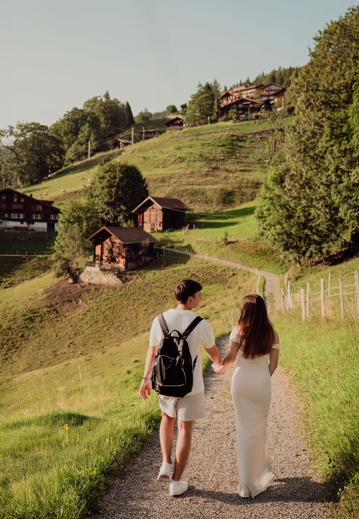 A couple strolls hand in hand down a winding path through a lush Swiss alpine hillside.