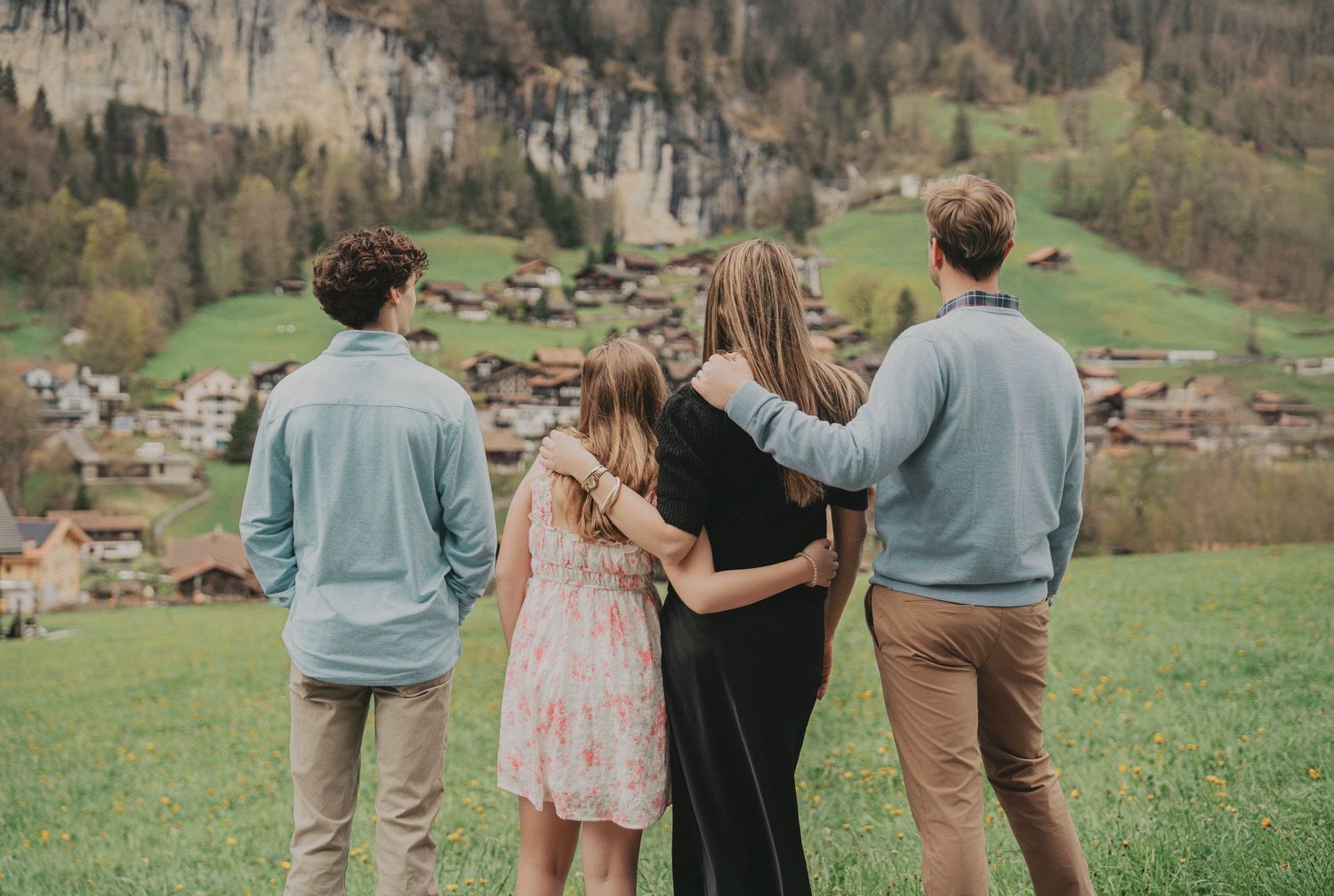 Family group embracing while overlooking charming Swiss mountain village nestled in alpine valley.