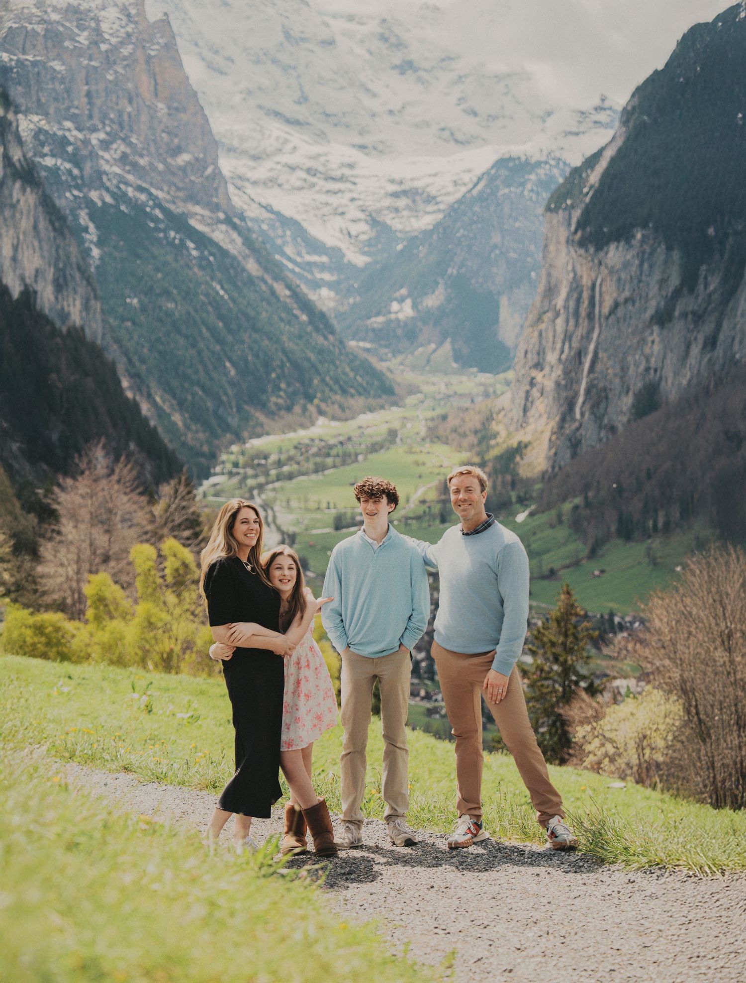 Family of four smiling on a scenic mountain path overlooking a lush Swiss Alpine valley.