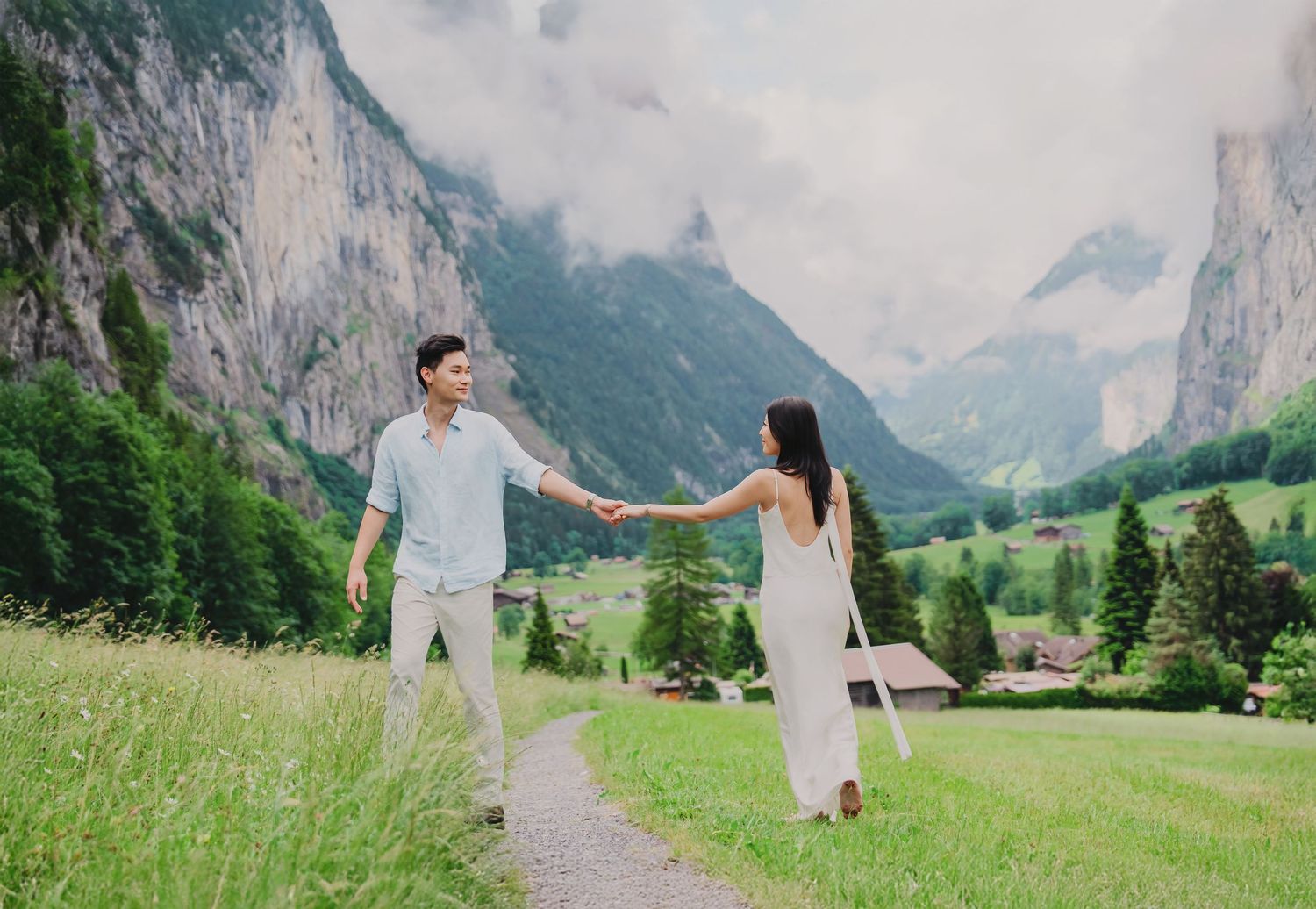 Couple holding hands on mountain path in Lauterbrunnen valley Switzerland with dramatic cliffs and green meadows.