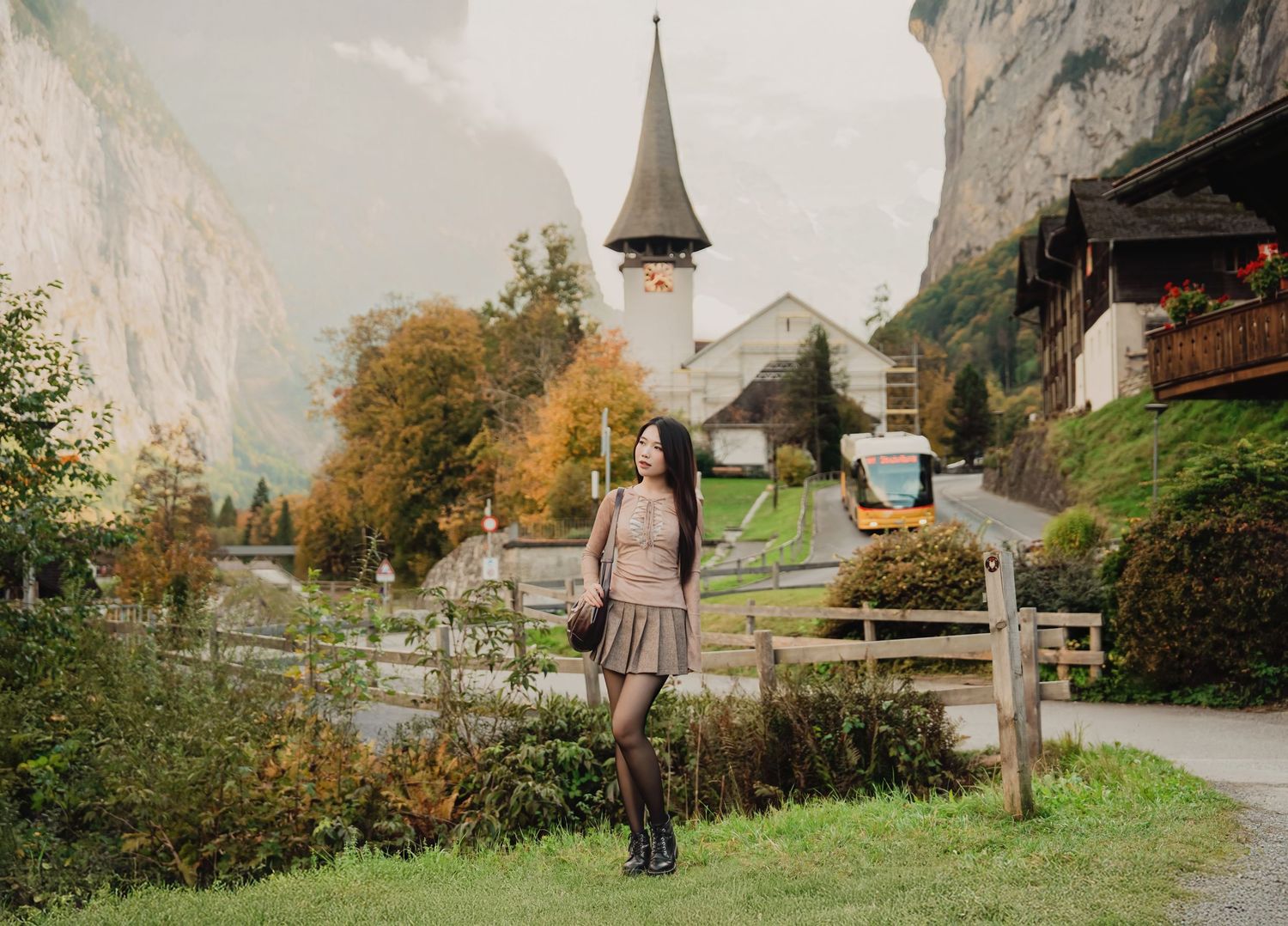 Young woman in skirt and boots posing near a church in a beautiful Swiss mountain village.