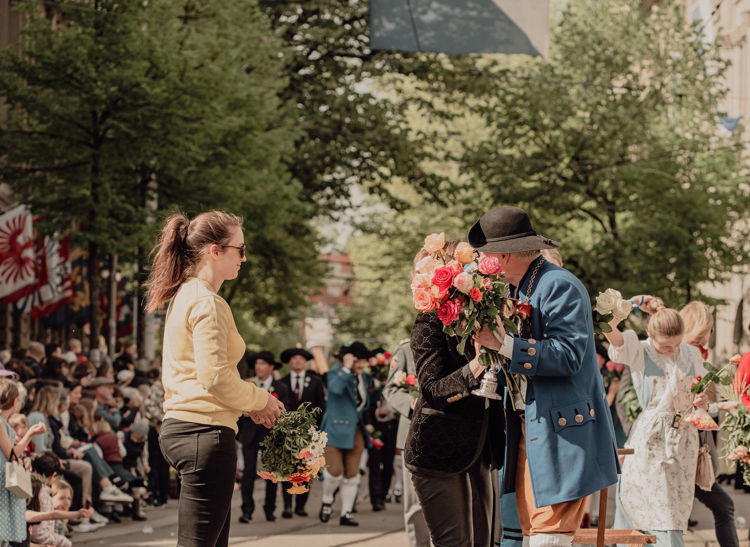 A man in historic costume bows while offering a large bouquet of roses to spectators at a parade.