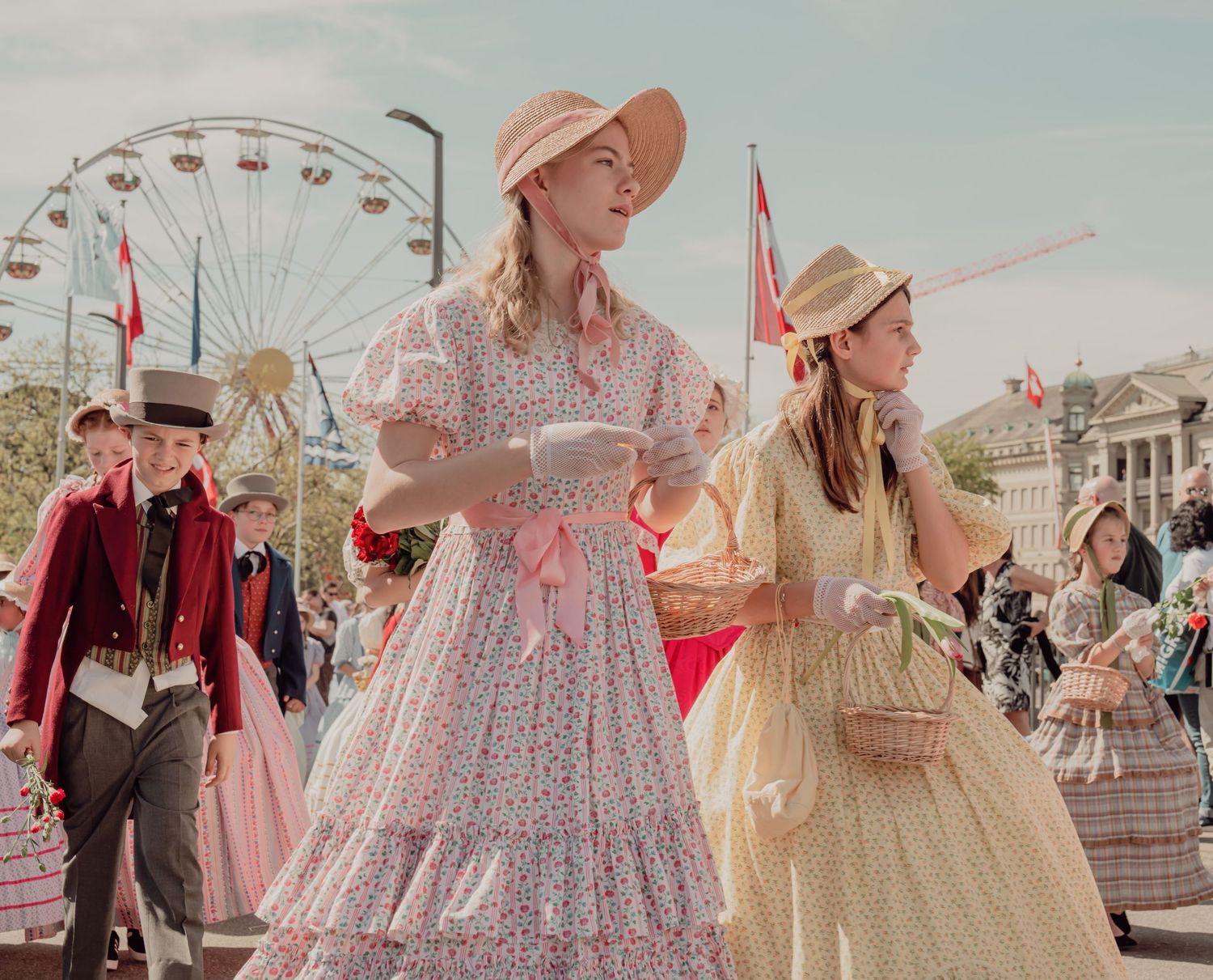 Young women in vintage floral dresses and bonnets walk in a sunny outdoor historical parade.
