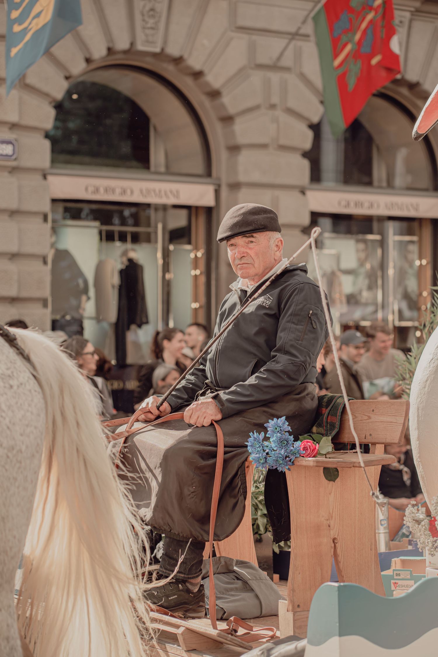 Elderly man in dark clothing riding a horse-drawn carriage during a traditional street parade near Giorgio Armani store.