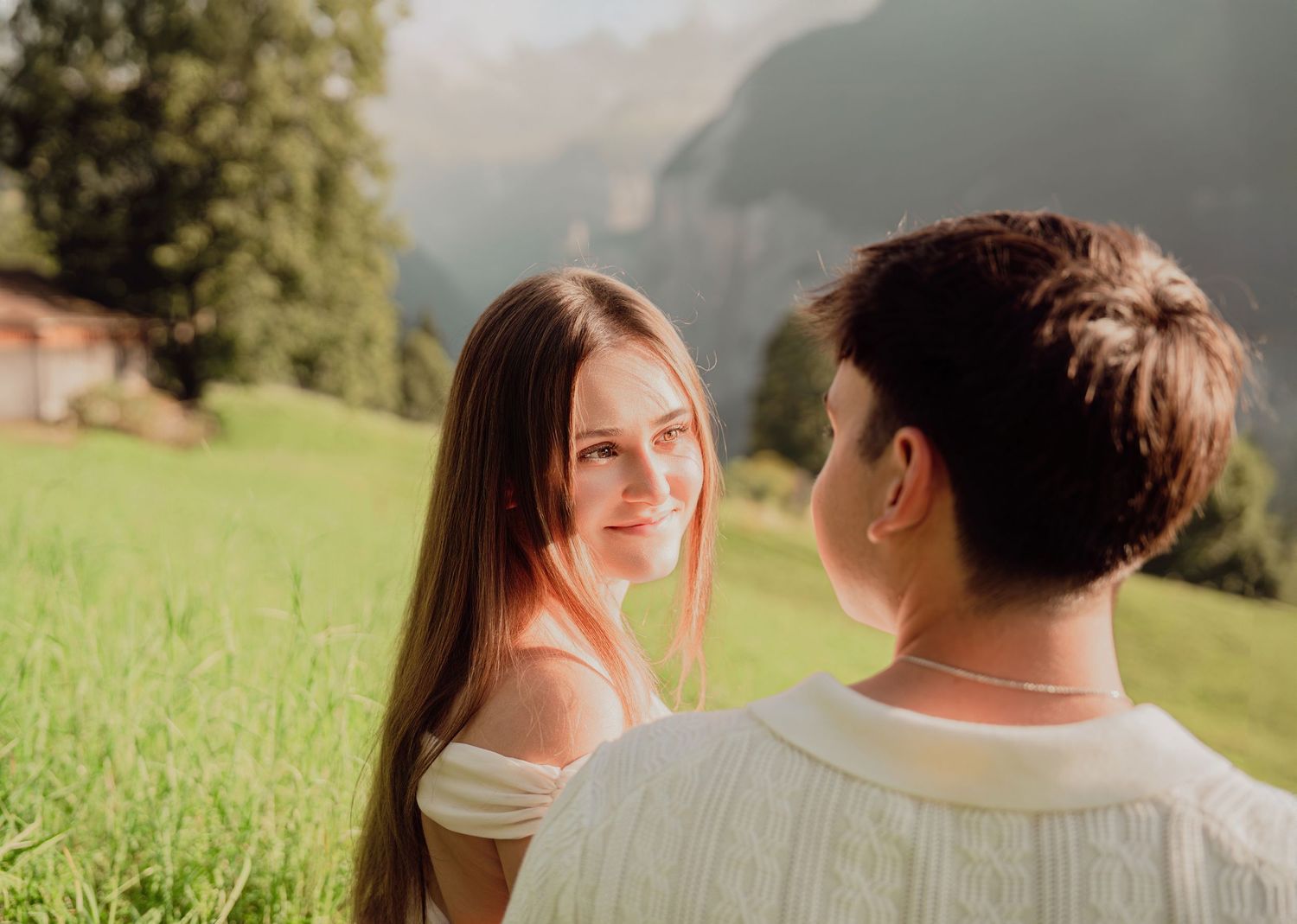 A couple shares a tender moment in a lush alpine meadow with mountains in the background.