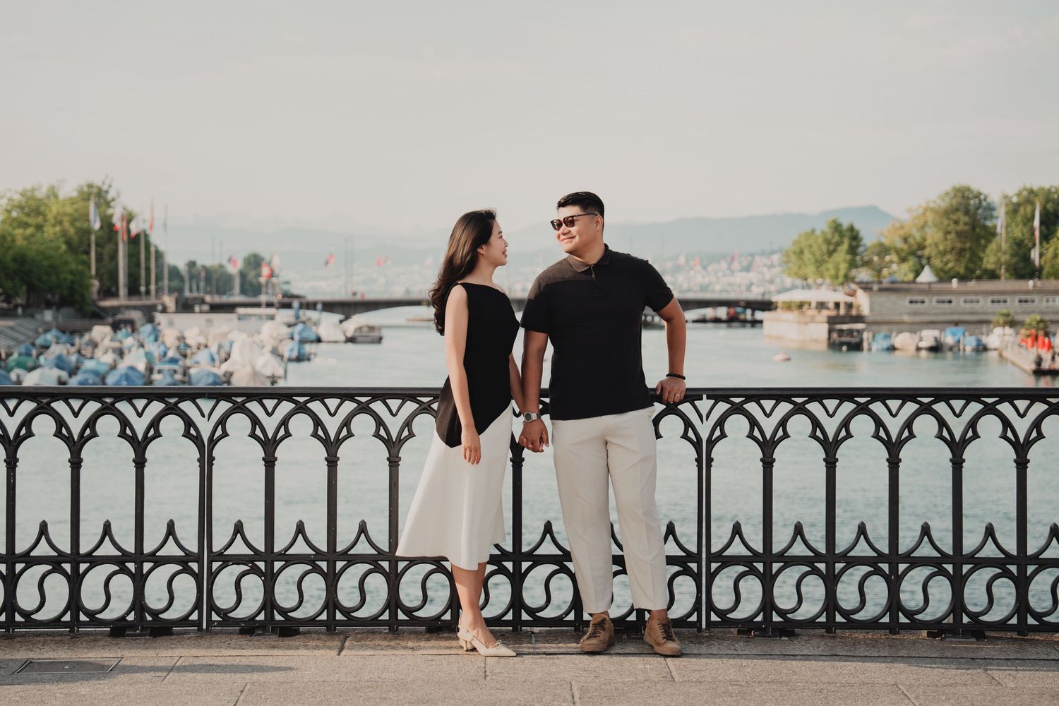 Couple in matching black outfits holding hands by iron fence at Zurich lakeside promenade.