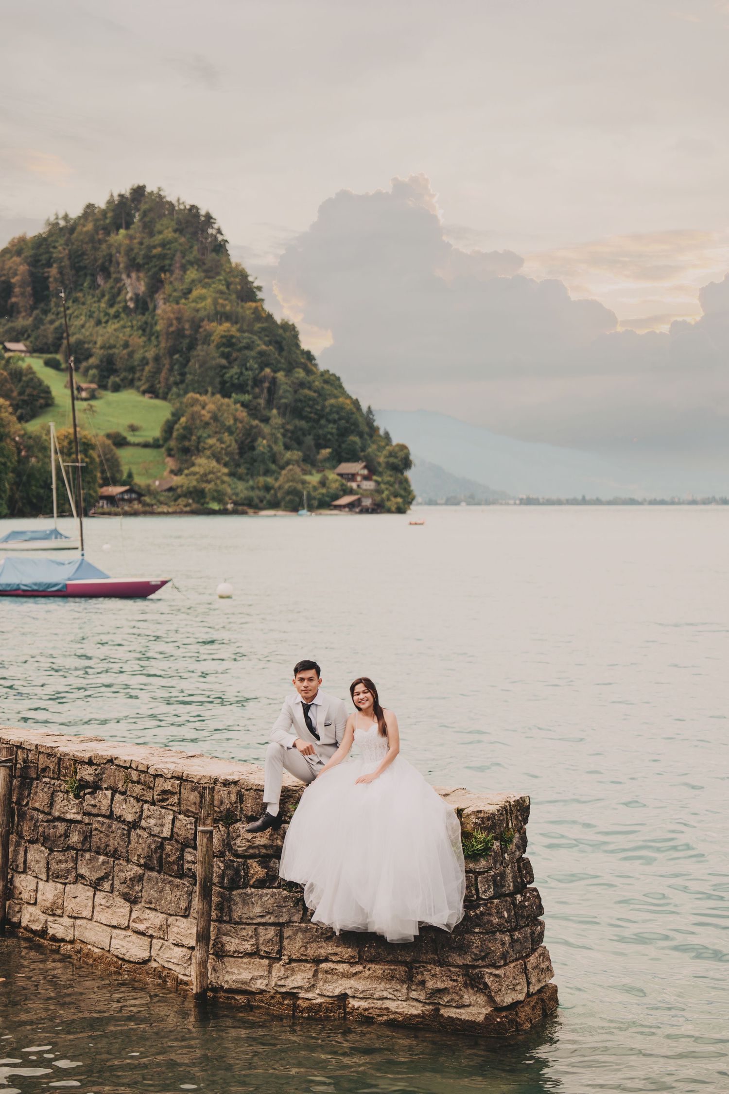 Wedding couple posing on stone dock overlooking serene alpine lake with mountain island background.