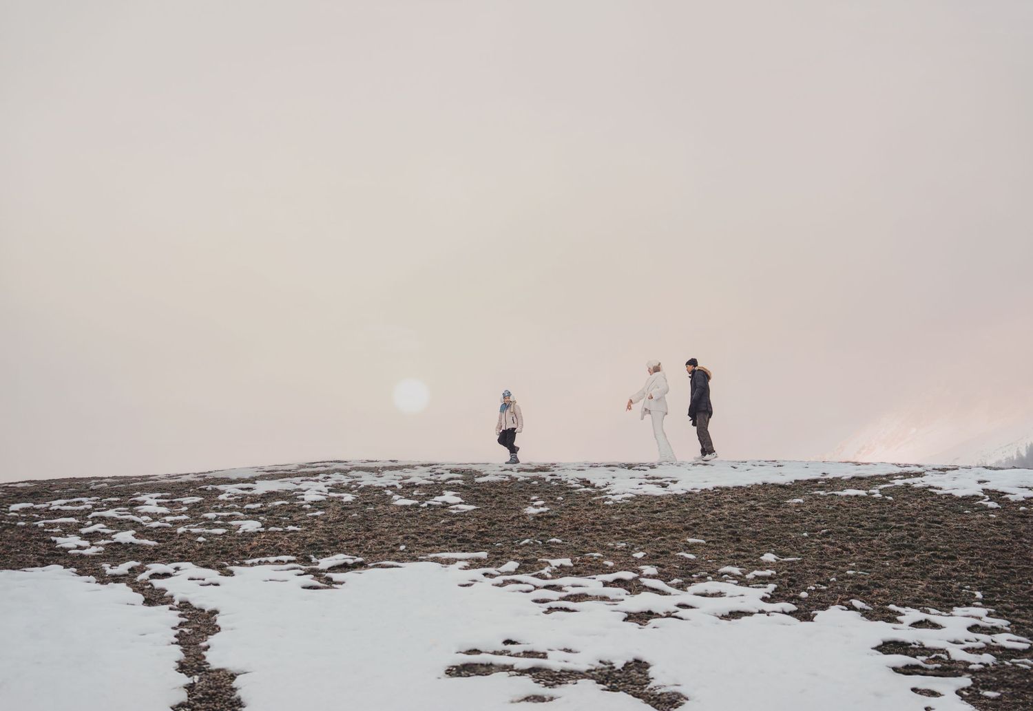 Three people walking along a snowy hilltop ridge in misty winter mountain conditions.