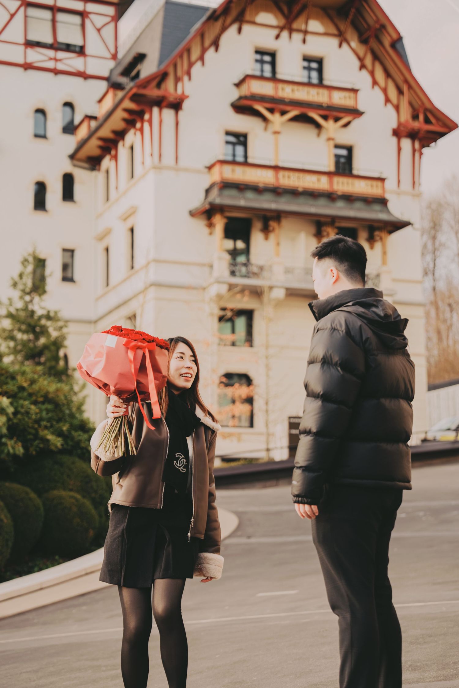 Woman holding red gift bag facing man outside ornate European building.