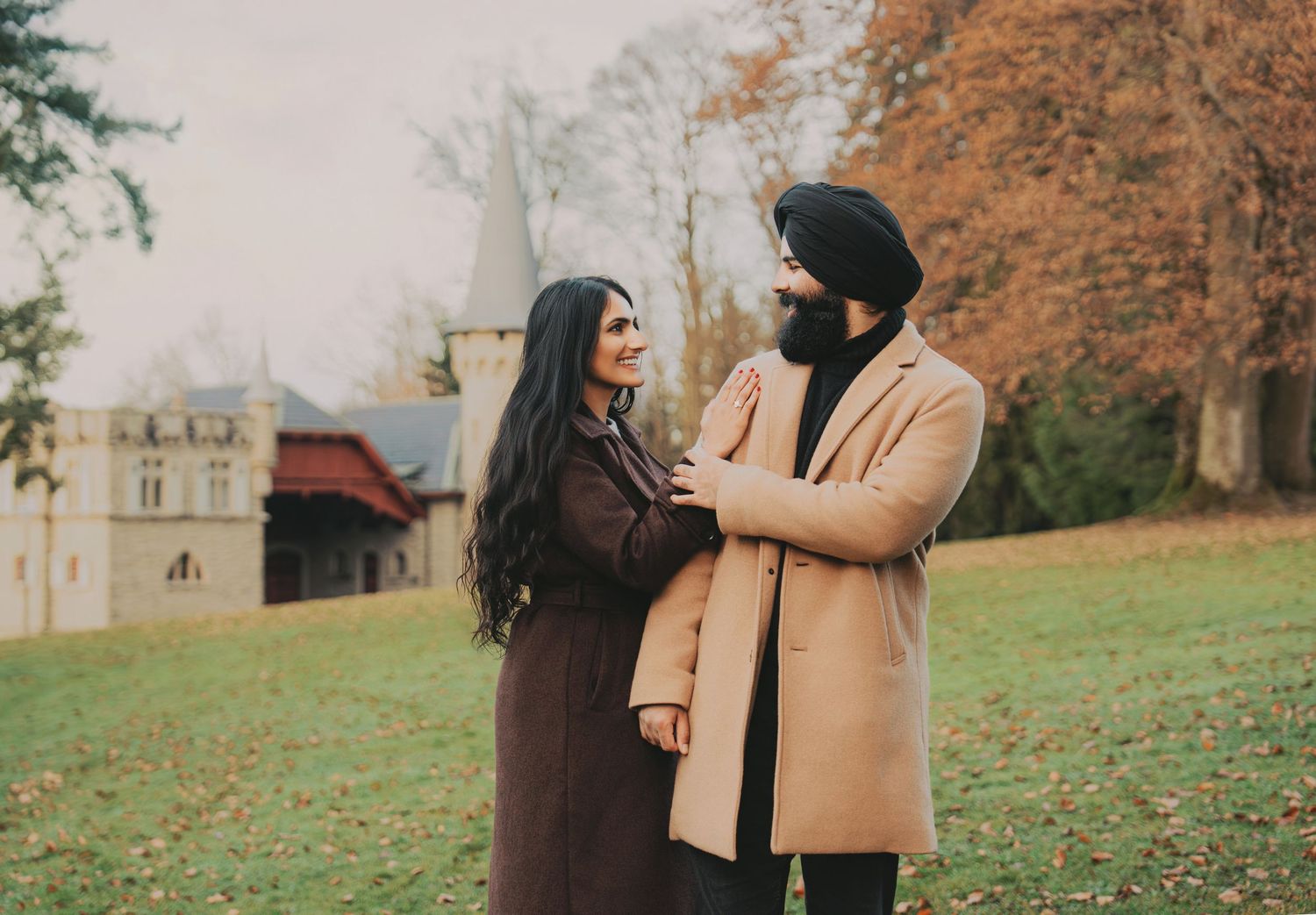 Couple gazing at each other while standing on a lawn with a castle in the fall background.