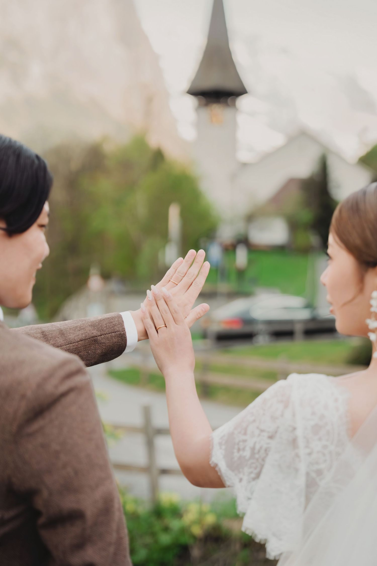 Close-up of bride and groom touching hands, showcasing wedding rings with a Swiss church in the background.