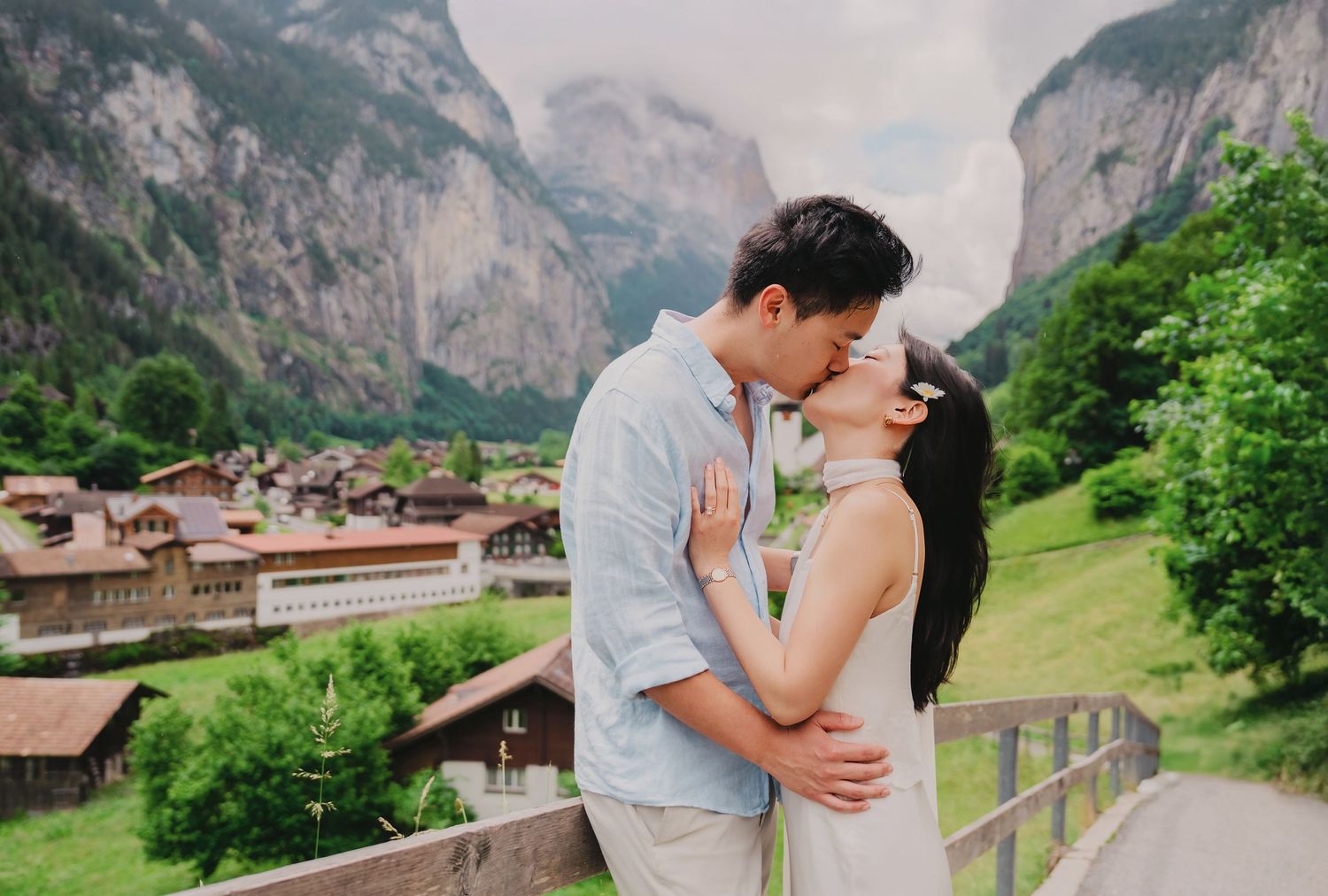 Couple sharing a romantic kiss with Swiss Alpine village and dramatic mountain waterfall backdrop.