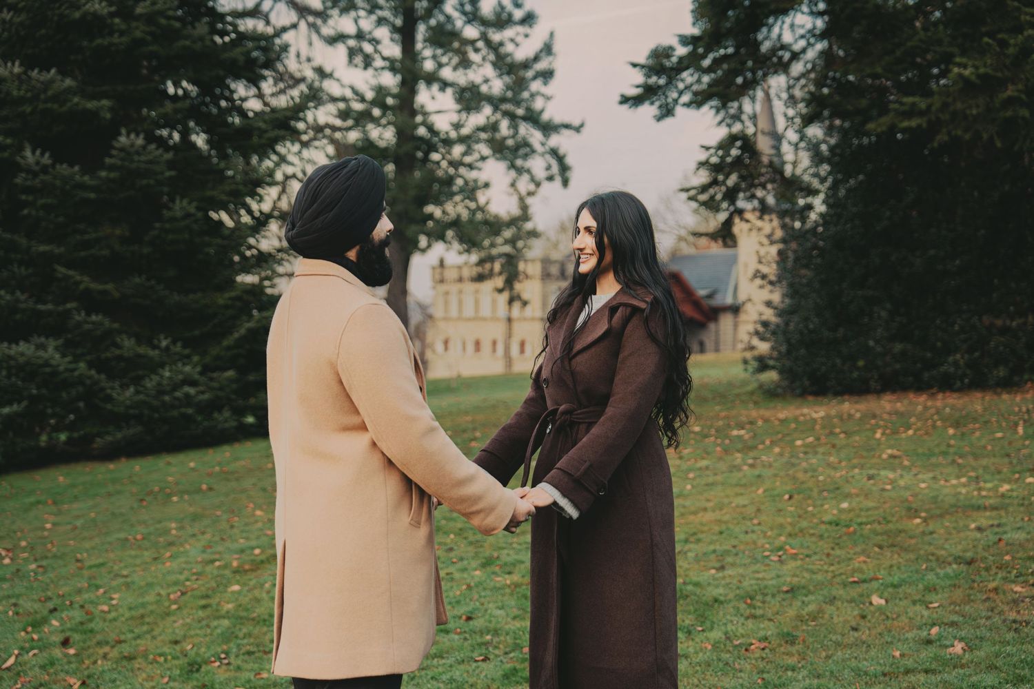 Couple holding hands facing each other in lush green park setting.