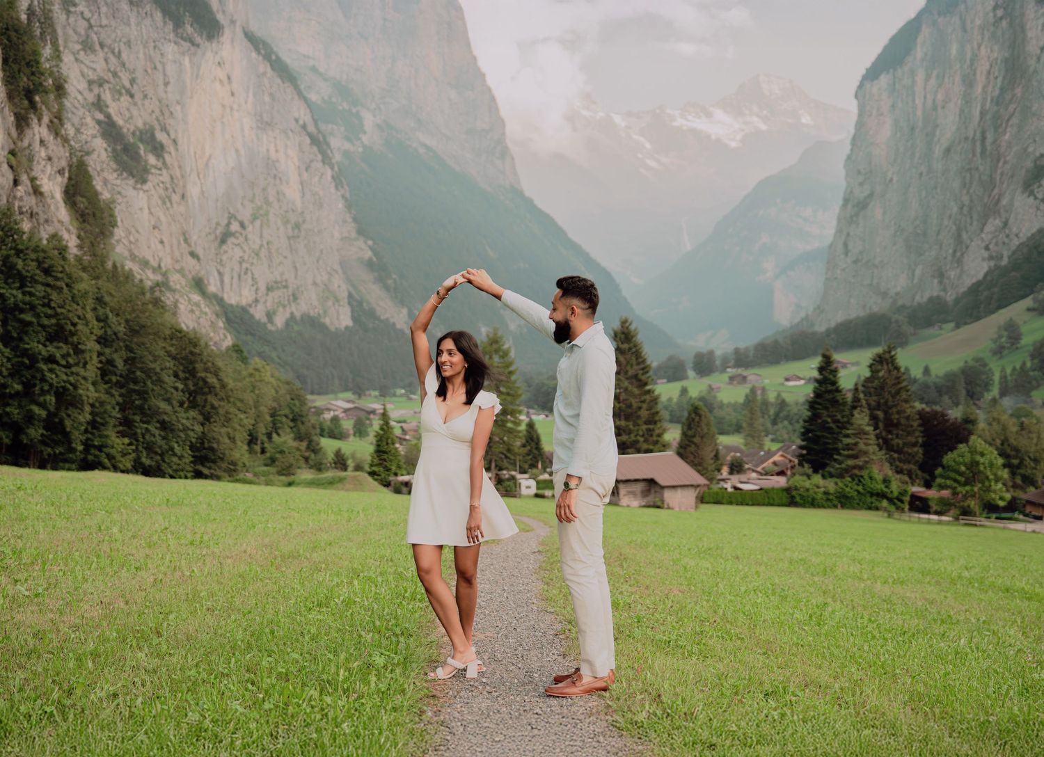 Romantic couple dancing on a path in a breathtaking Swiss Alpine valley surrounded by green meadows.