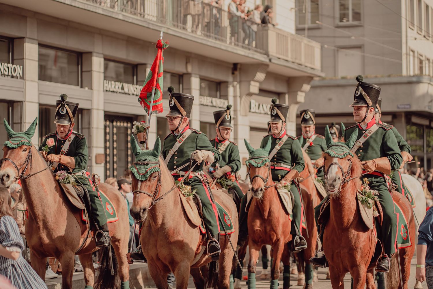 Soldiers in green Napoleonic uniforms riding brown horses in a historic parade.