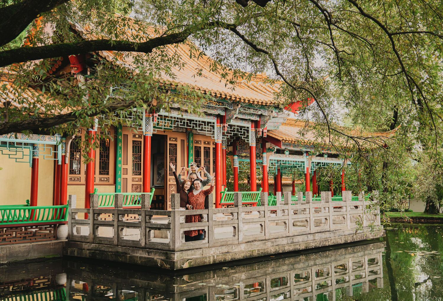 Traditional Chinese pavilion with vibrant red columns and decorative roof reflecting beautifully in a calm garden pond.