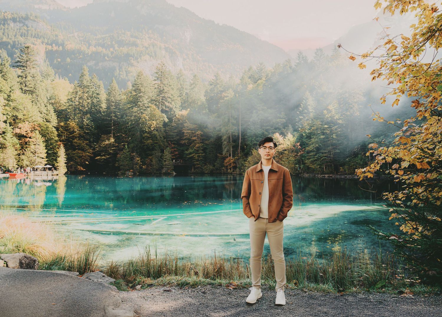 Man standing confidently before a stunning turquoise alpine lake with misty forested mountains.
