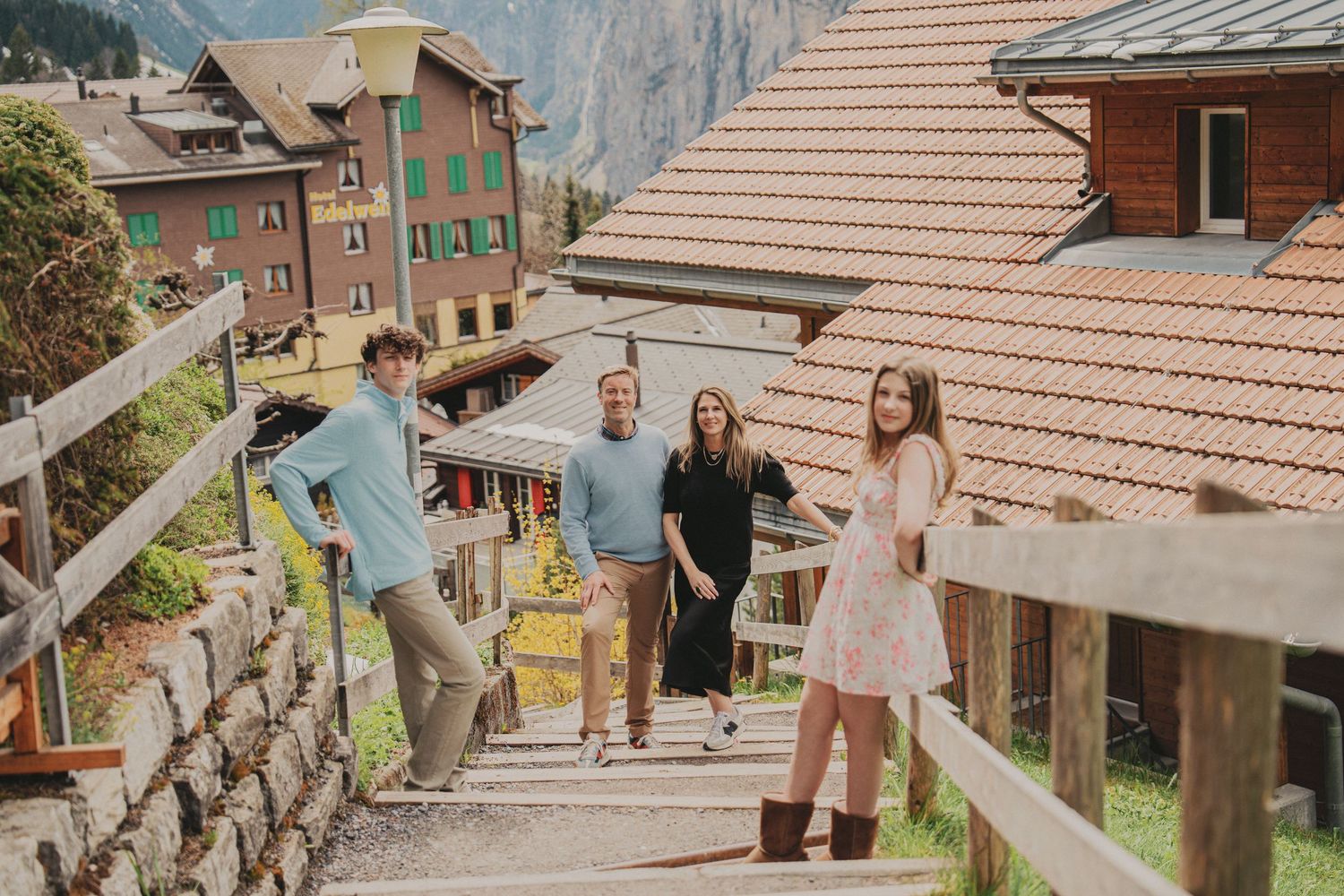 Family of four walking down wooden steps in a picturesque Swiss alpine village with mountains behind.