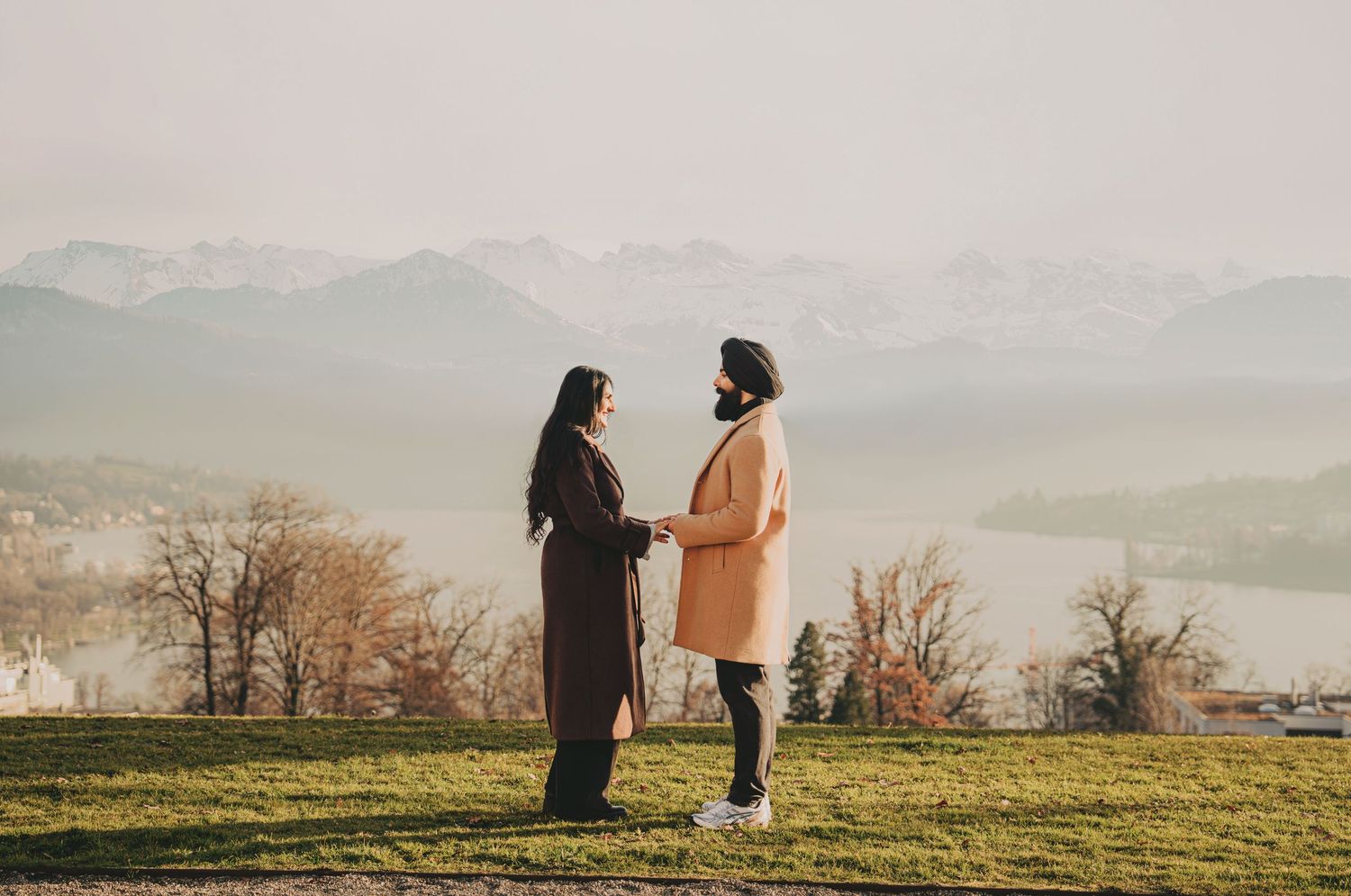 South Asian couple facing each other holding hands on a hilltop with foggy mountain landscape.