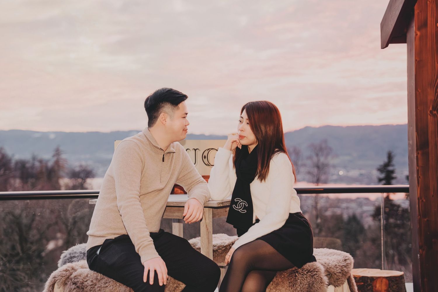 Young couple sitting together on terrace at sunset with scenic cityscape in background.