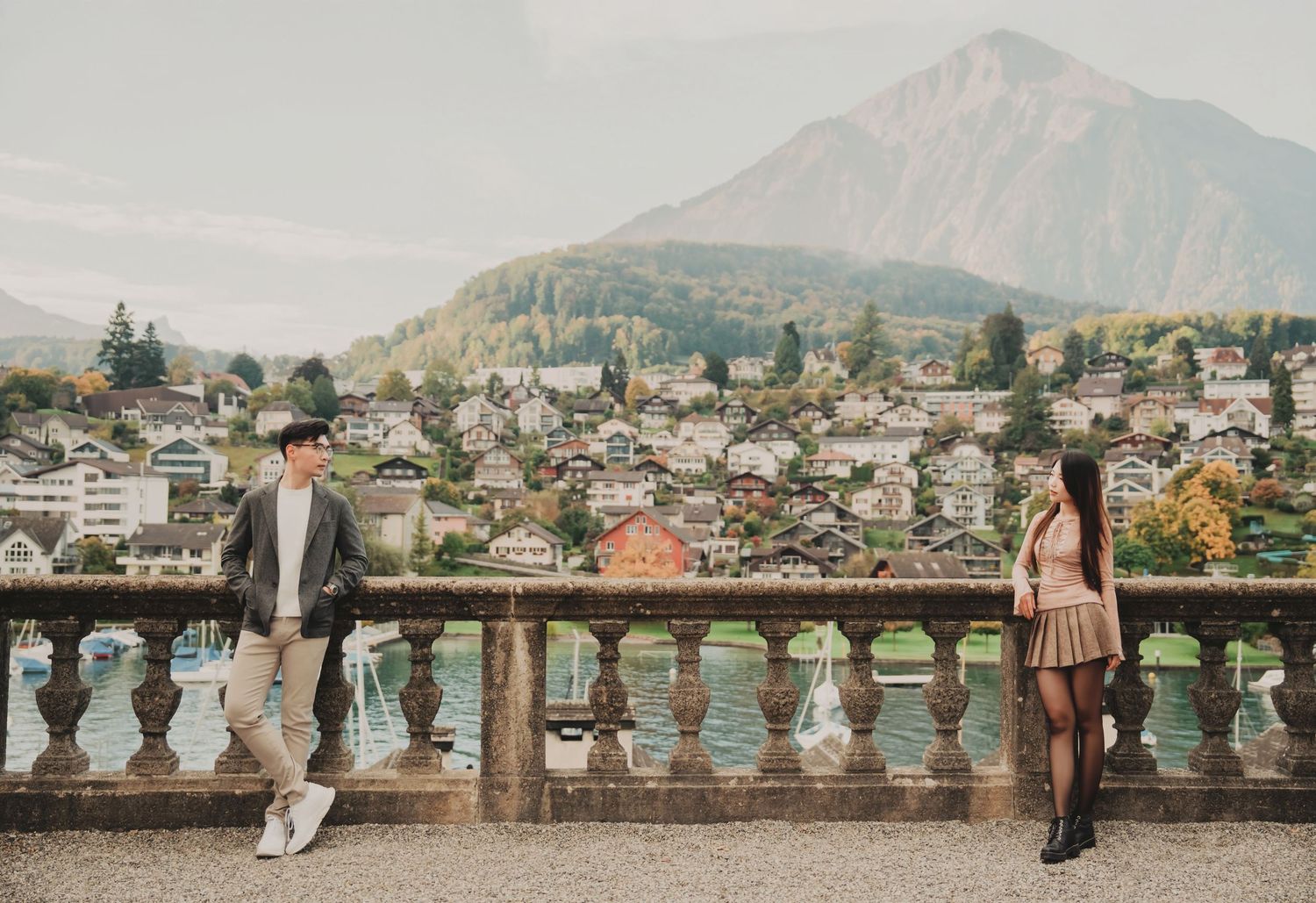 Couple standing apart on a stone terrace with a scenic Swiss mountain town backdrop.