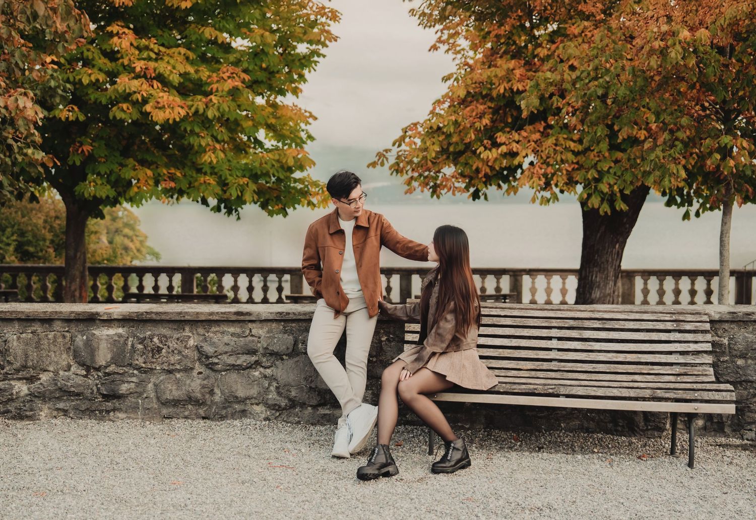 Asian couple interacting playfully on a bench surrounded by vivid orange and yellow autumn trees outdoors.